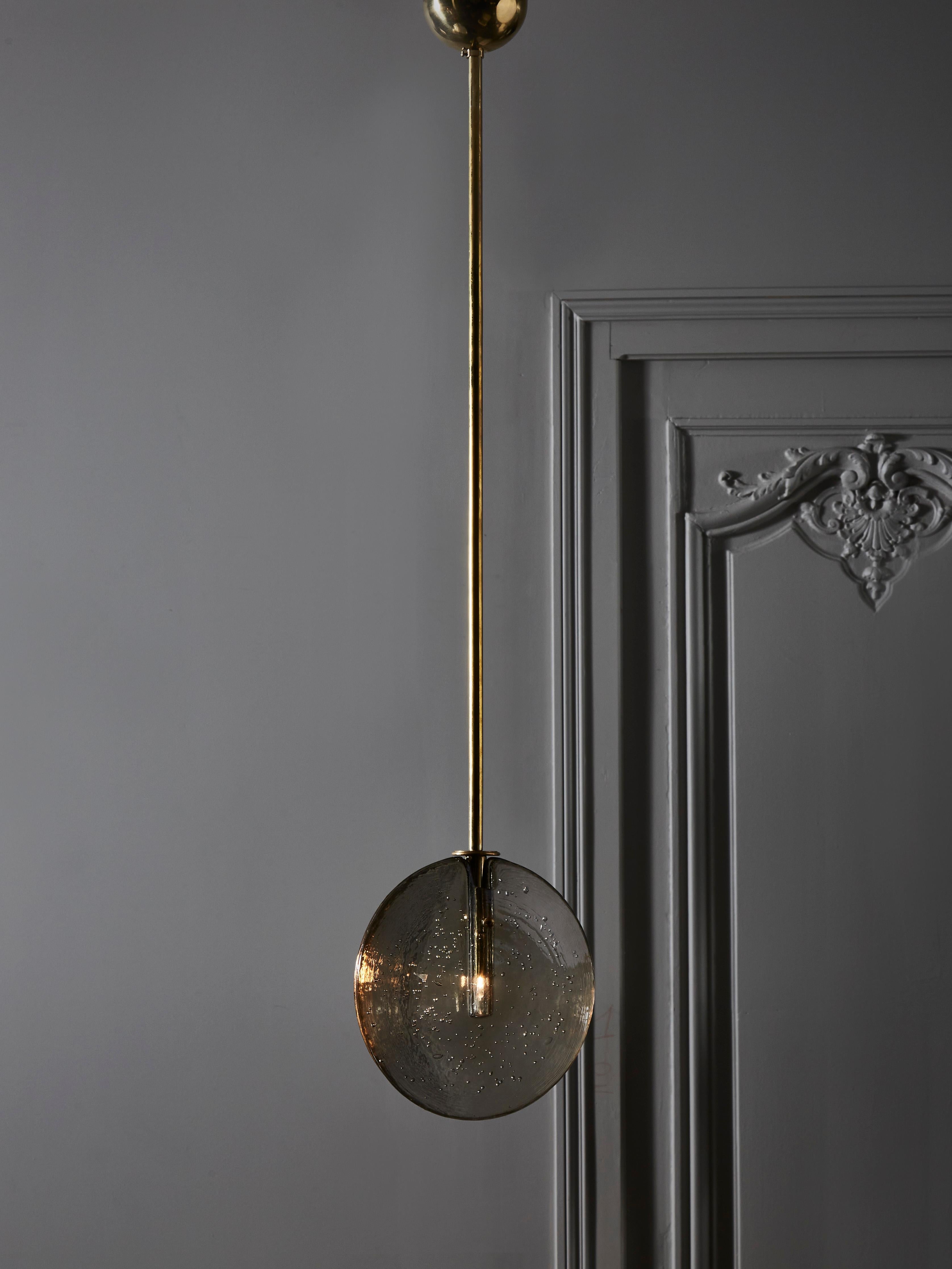 Chic and simple suspension made of a brass stem holding a disc of bubbled and tinted glass, enclosing a single light bulb.