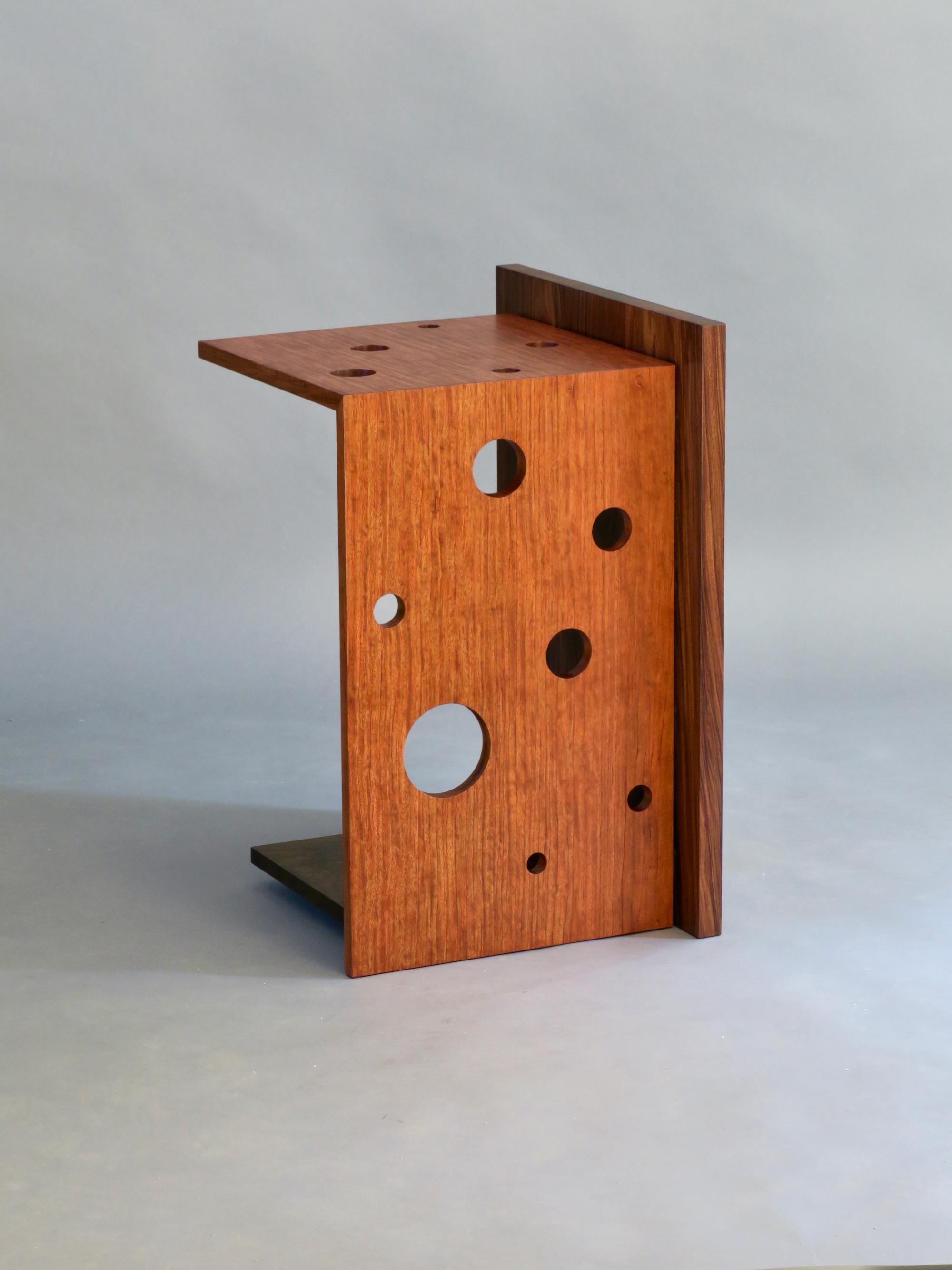 The Oriel VI side table features a cantilevered top and waterfall joined leg in highly figured bubinga which has been perforated with round 
