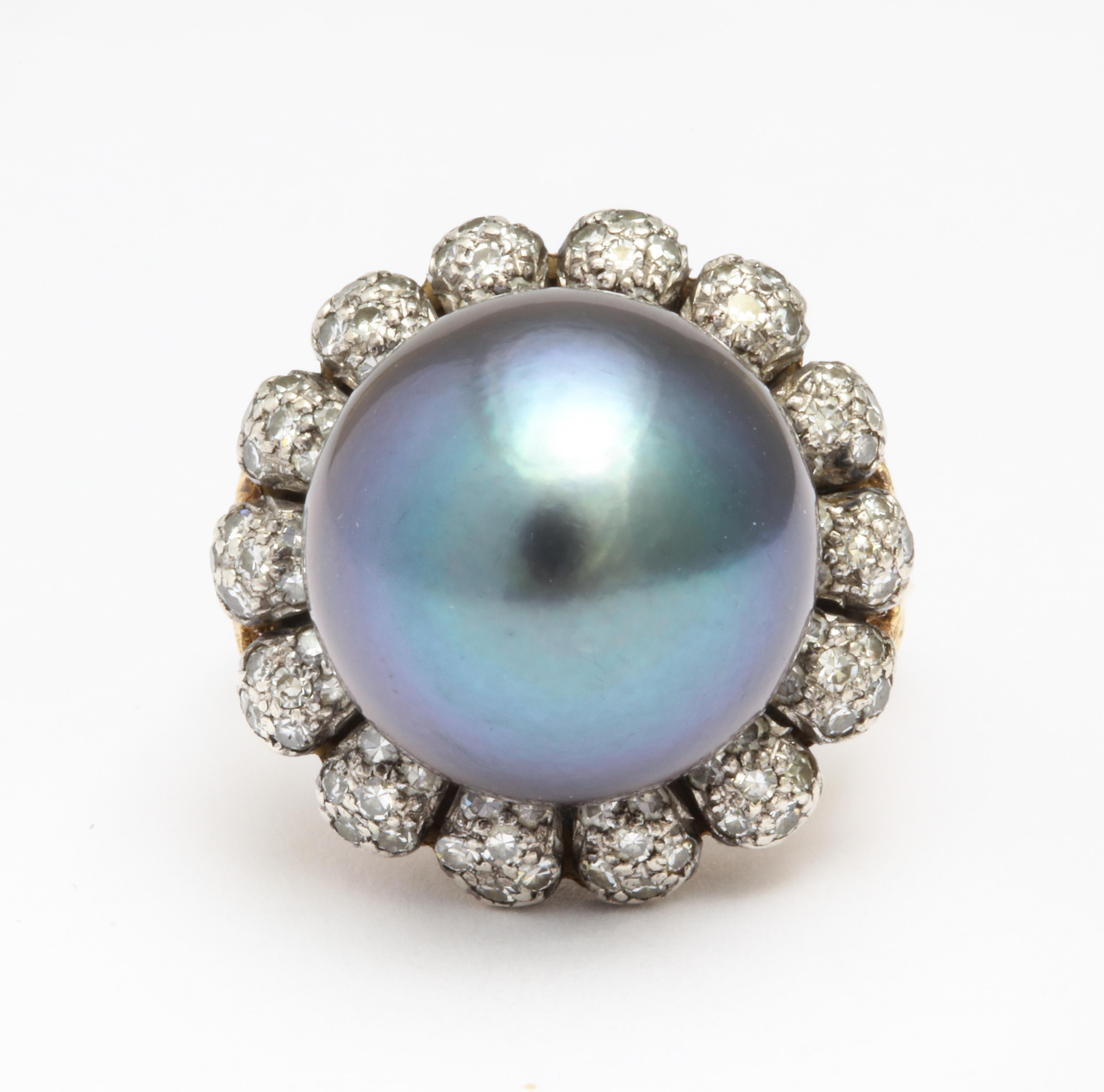 A beautiful 14mm Tahitian Pearl with aubergine tone and incredible luster is the center of this 18K yellow gold ballerina ring.  It's surrounded by a row of 14 demure old mine cut diamonds, with an estimated total weight of 0.50 carats. 
Size 6