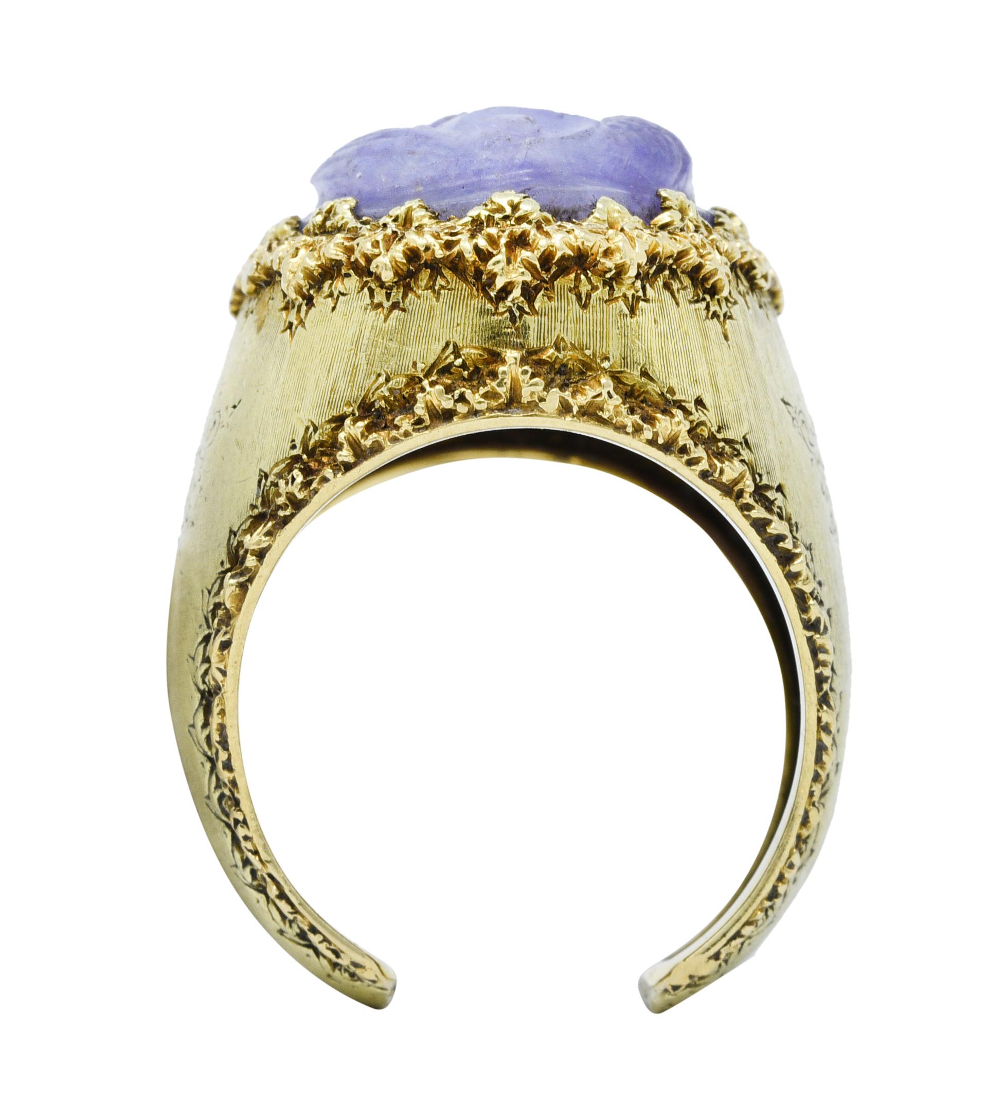 Centering oval cut lavender jade measuring approximately 18.0 x 14.0 mm

Translucent, mottled, and deeply carved to depict a stylized serpent dragon

Edges of ring are comprised of a texturous foliate motif

Completed by a wide band with an open