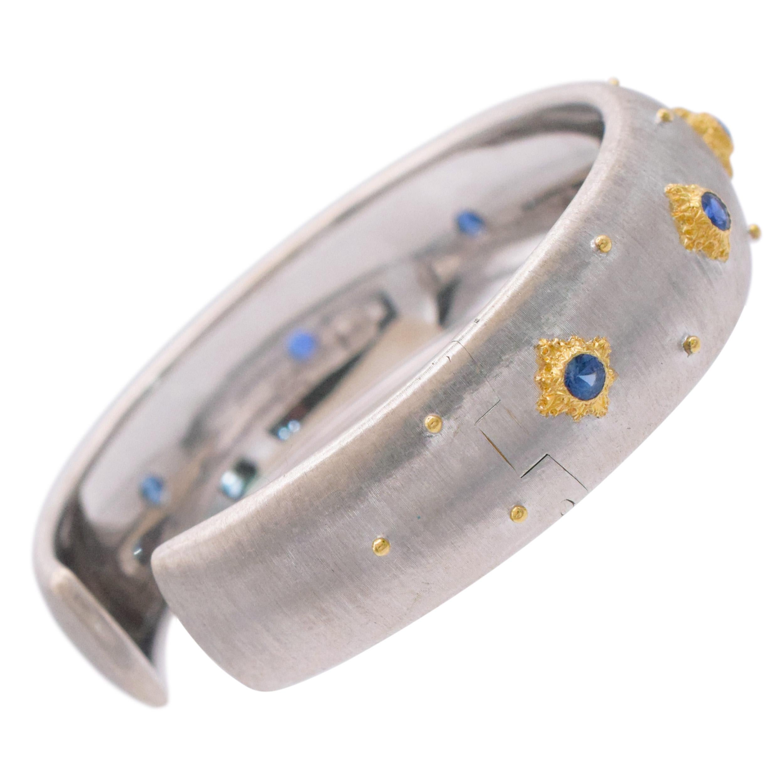 Buccellati Macri white gold cuff braclet with sapphires. The bracelet is crafted in 18k white gold with signature Buccellati brushed finish.
Accented with 7 round cut blue sapphires, bezel set in 18k yellow carved gold decorative frames. The