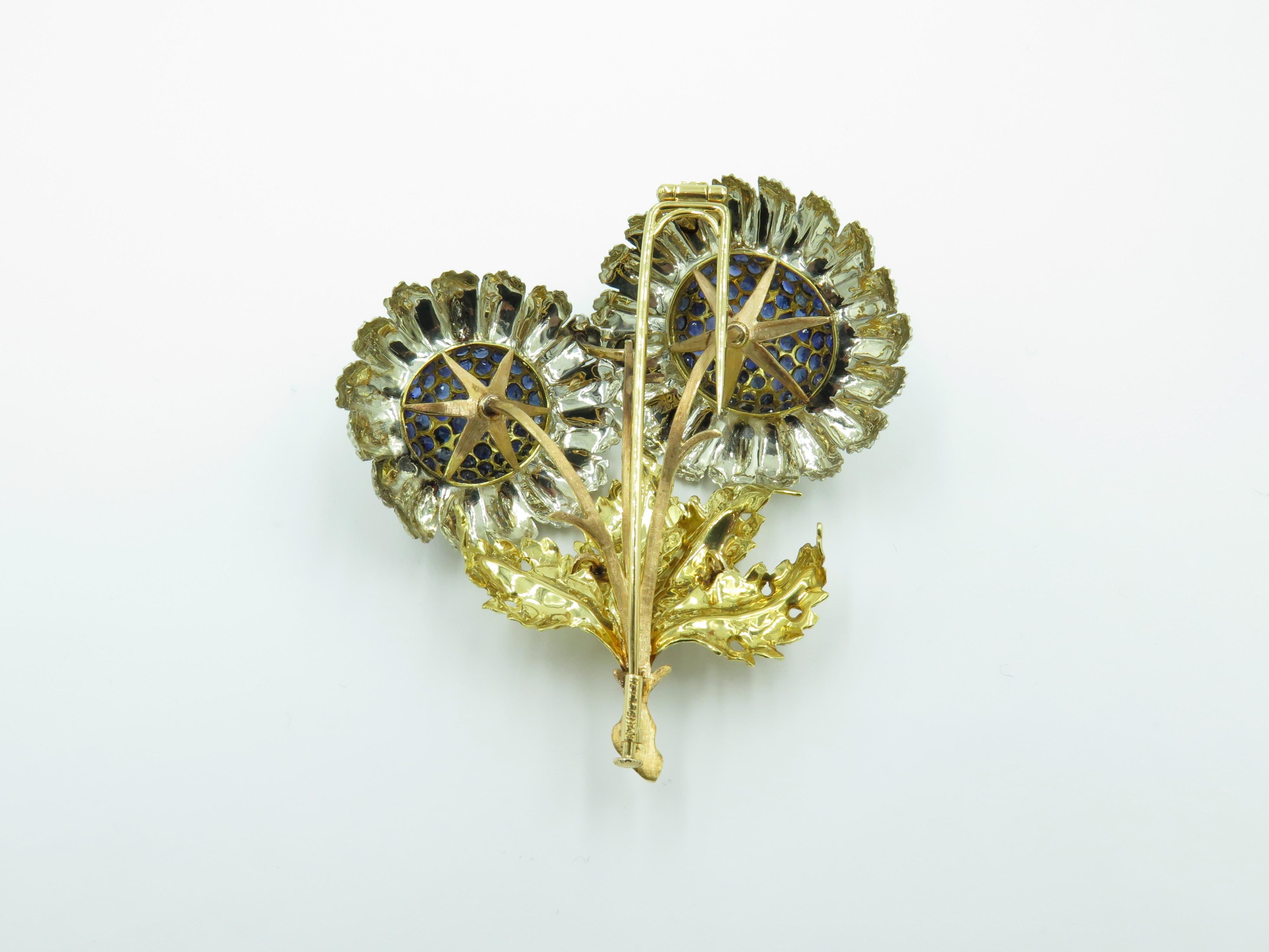 An 18 karat yellow gold, white gold and sapphire brooch. Buccellati. Circa 1960. Designed as two daisies, extending textured white gold petals, with pave sapphire centers,  with textured gold stem and leaves. Length is approximately 2 3/4 inches,