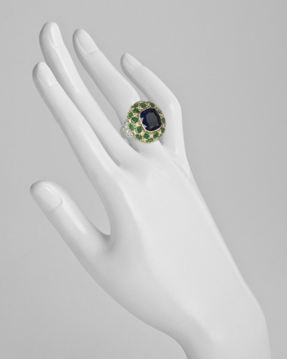 Cocktail ring, centering a cushion-shaped natural sapphire within a bombé-style mount of pavé-set emeralds and diamonds, in a textured 18k white gold setting with 18k yellow gold, signed Buccellati.
 
Sapphire weighing ~8.00 carats
Emeralds weighing