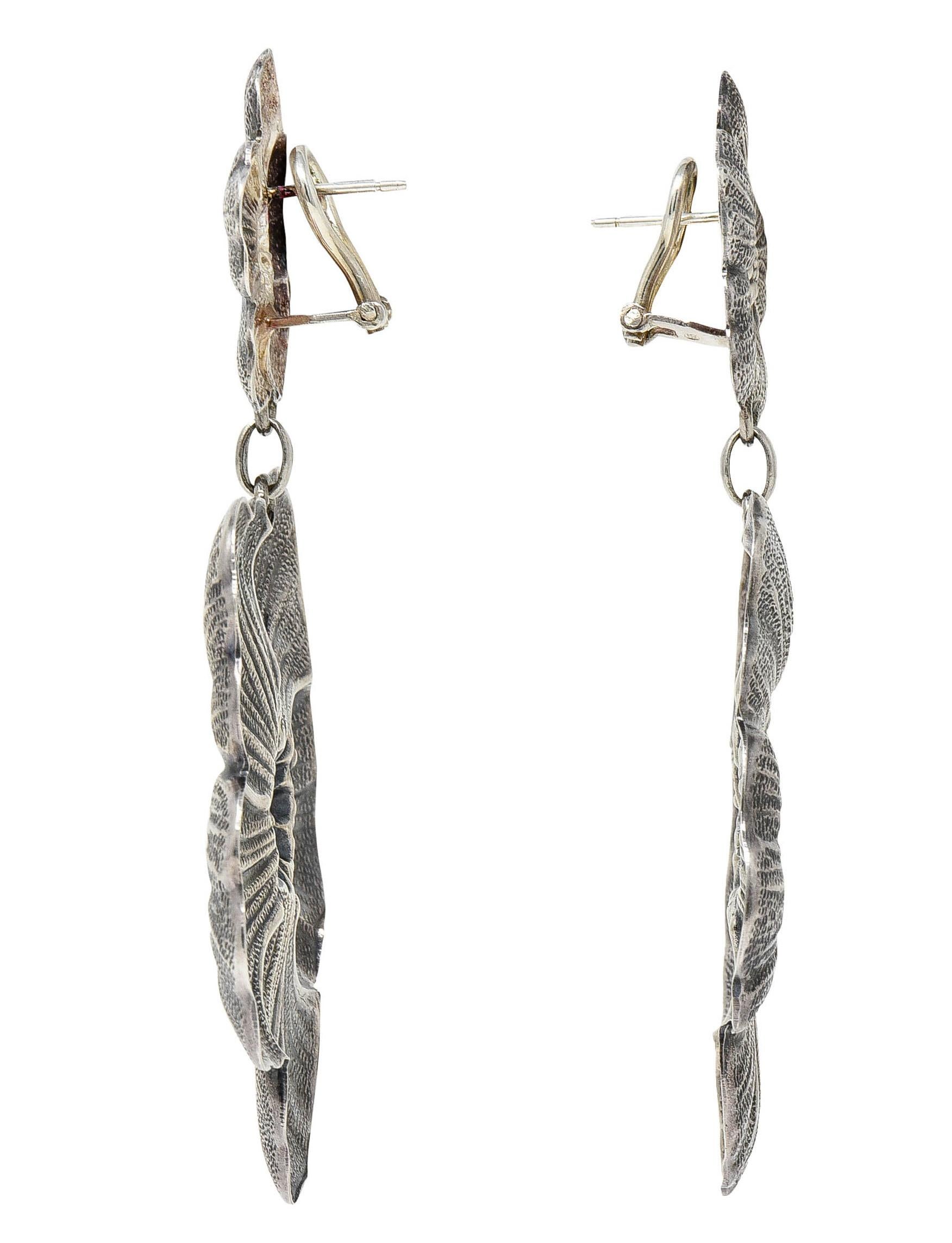 Designed as repoussè rendered gardenia blossoms

With a smaller blossom surmount suspending an articulated larger blossom drop

Featuring intricate petal veining and a clustered center

Completed by hinged omega backs

Stamped Sterling for sterling