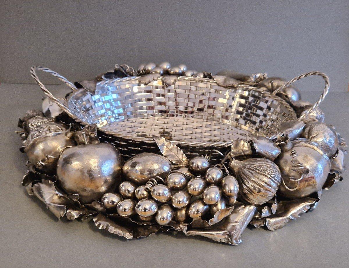 Centro de mesa de plata de ley de la Maison Buccellati Compuesto por una cesta tejida con dos asas, rodeada de frutas naturales: fresas, manzanas, granadas, racimos de uvas, melocotón, limón, higo sobre un lecho de hojas.
Sello de platero: M.