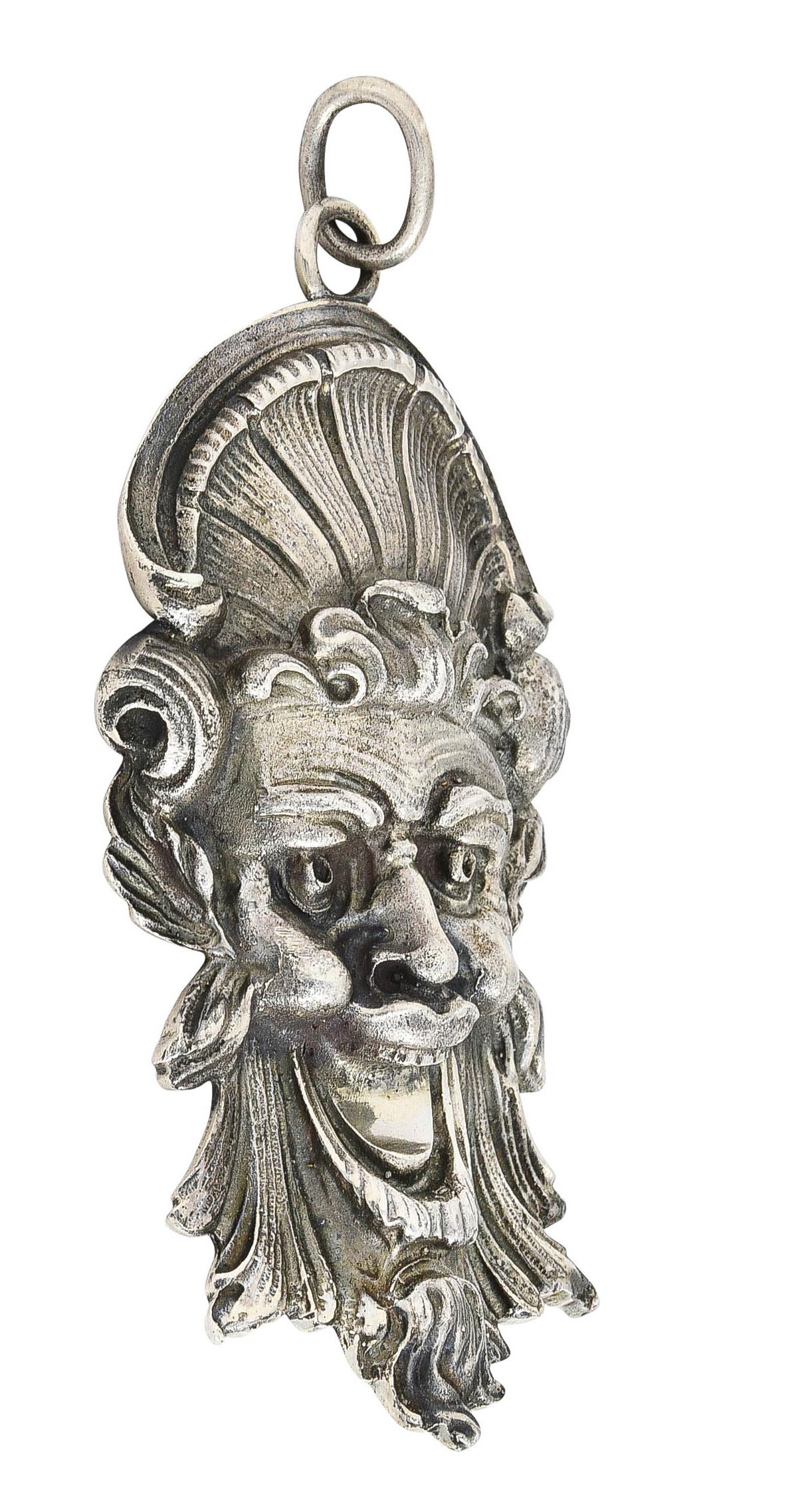 Designed as a highly rendered face of a man with an exaggerated jolly expression. Wearing a fanning headdress with grooved sweeping hair and beard. With oxidized patina throughout. Completed by large jump ring bale. Stamped sterling for sterling