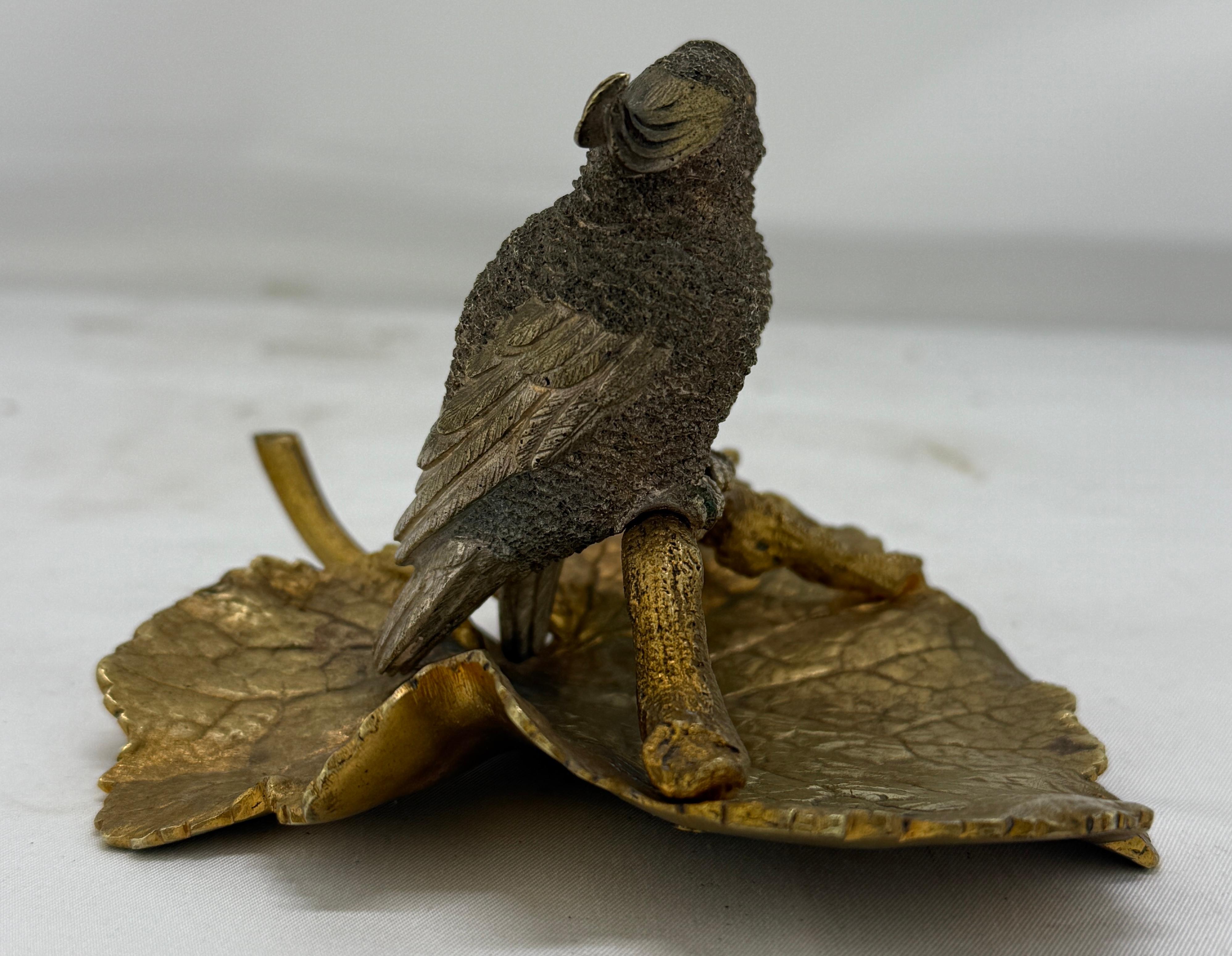 A finely cast and naturalistically modeled bronze figural sculpture depicting a pair of cockatoos perched side-by-side on a sinuous, gilt branch, which curves gracefully across a broad repoussé leaf-form base. The birds, captured in tender profile