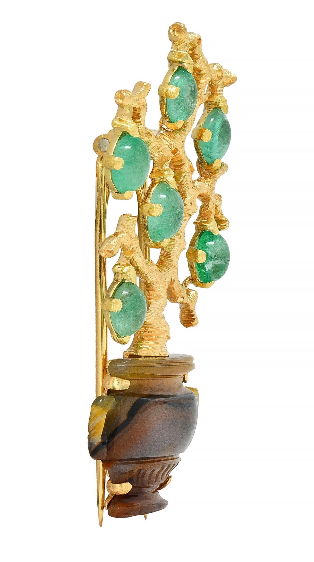 Designed as a potted gold tree with organically textured branches suspending emerald cabochon fruits
Weighing approximately 2.70 carats total - transparent light green in color and prong set
Pot is made of carved agate with engraved details and