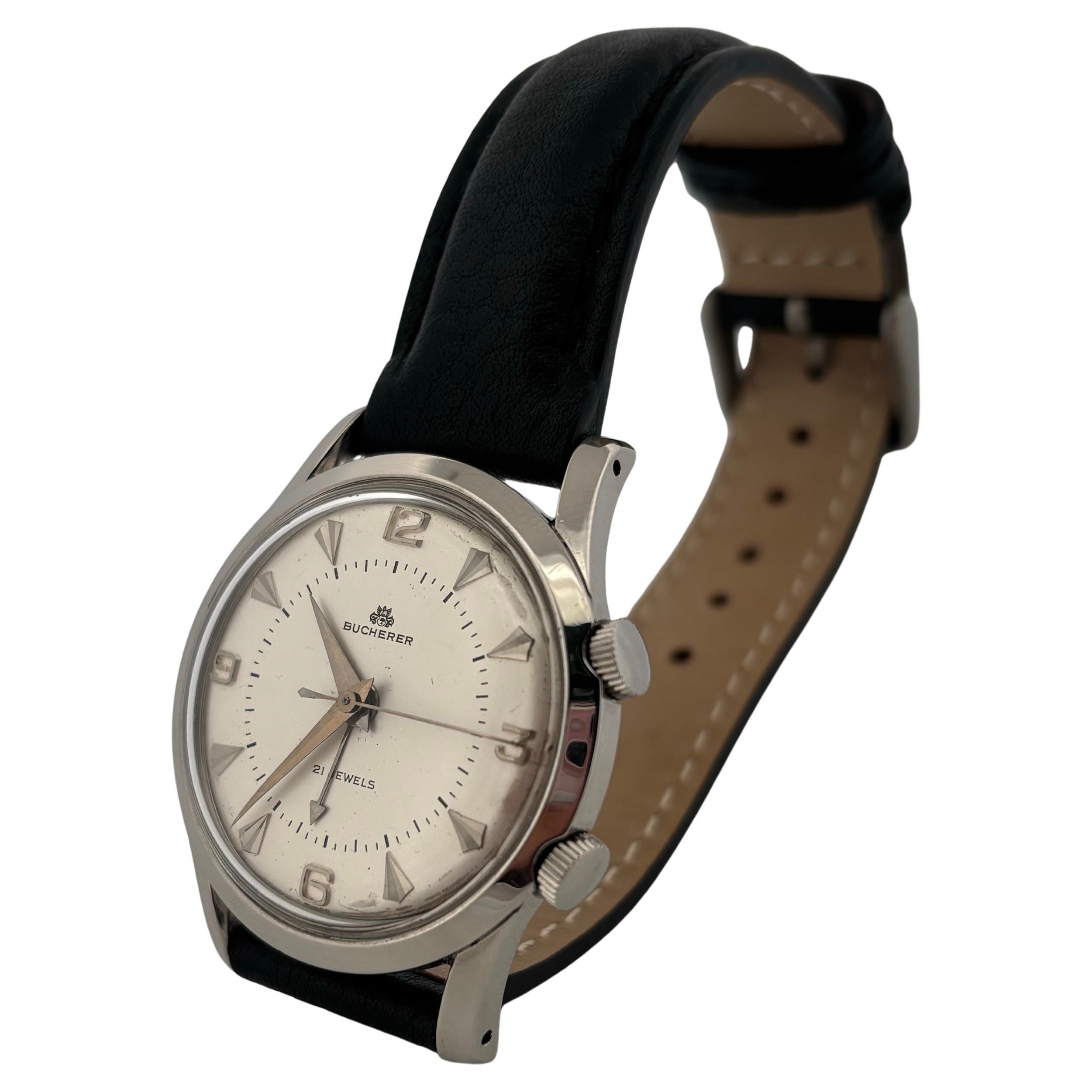 This vintage Bucherer stainless steel alarm wristwatch from the 1970s is a fine example of Swiss ingenuity and design. Measuring 34 millimeters in diameter, the watch features a clean silver-tone dial with applied Arabic numerals at 12, 6, and 9,