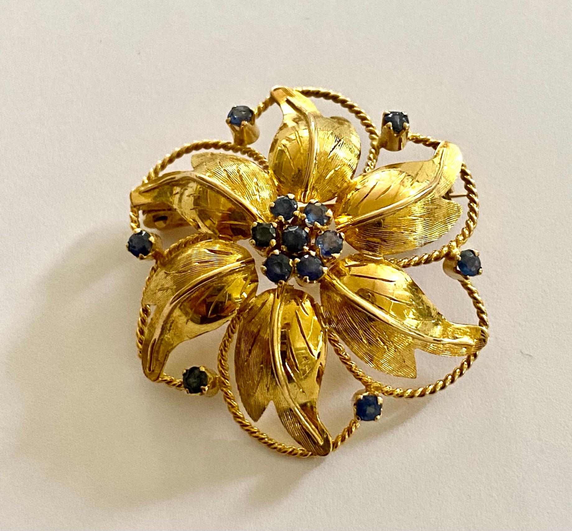 An 18K. yellow gold floral brooch, round model made of six leaves and 13 sapphires.
Signed: CB = C. Bucherer in Switzerland
Made in ca 1960
Weight: 9.29 grams
Dimensions: 35 mm round, and 9 mm. high
Equipped with a safety closure.