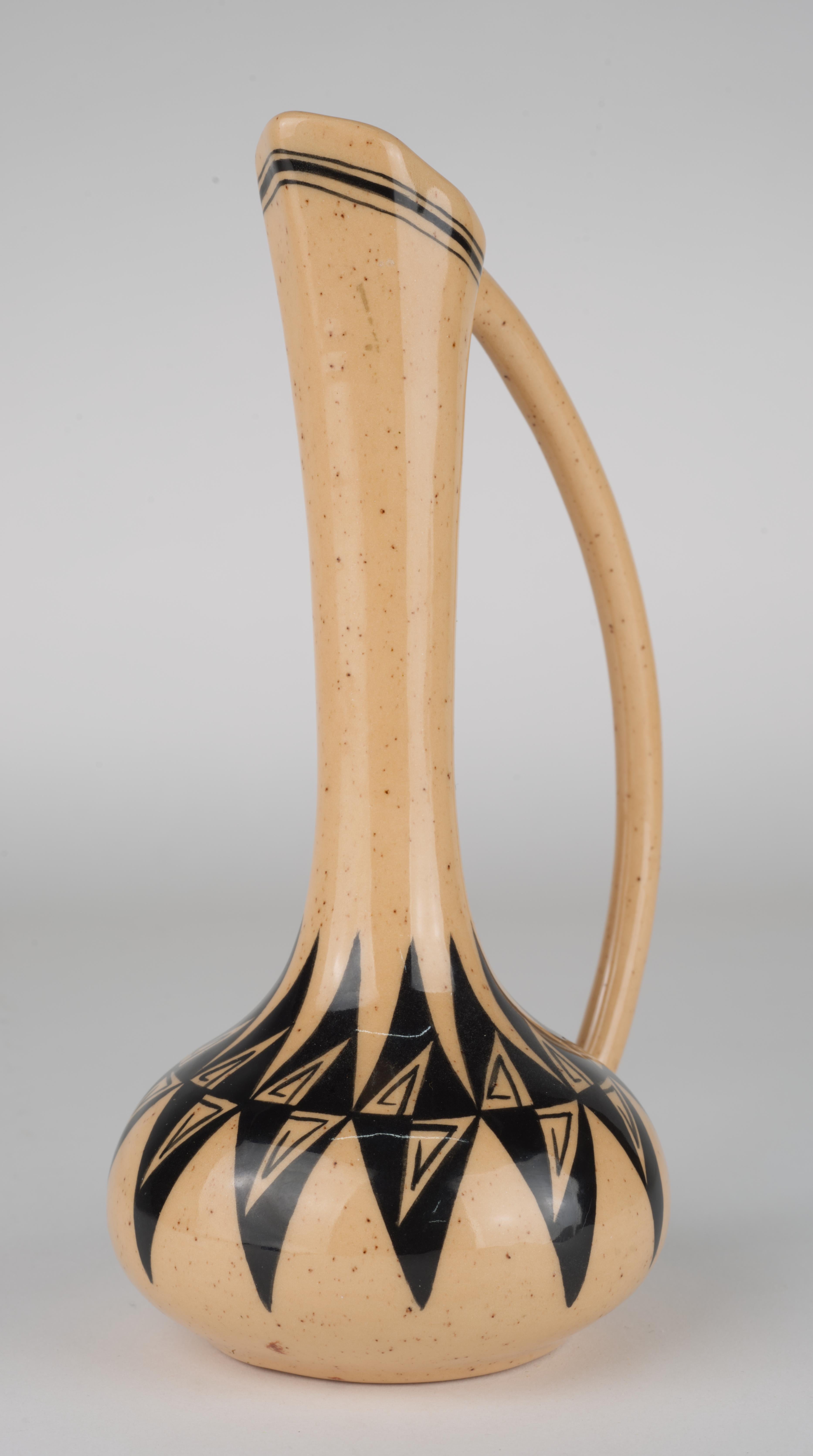  Ce gracieux vase en forme d'aiguière est tourné et décoré à la main d'un motif abstrait traditionnel en noir sur fond de glaçure rose corail tachetée. L'emplacement du motif est proportionné de manière sensible à la forme du vase, créant un effet