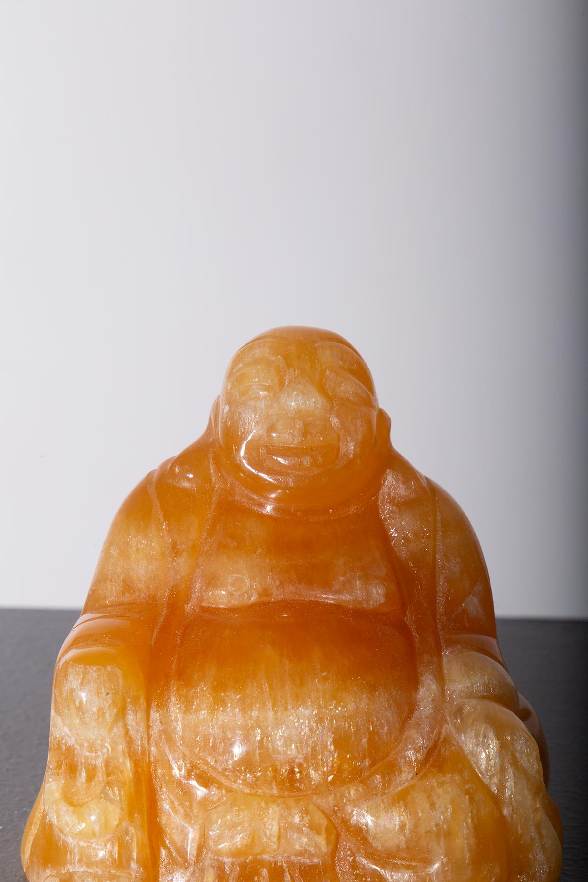 This fascinating sculpture of Budai, crafted from precious orange jade, exudes a sense of serenity and joy. With his welcoming smile and relaxed posture, the 