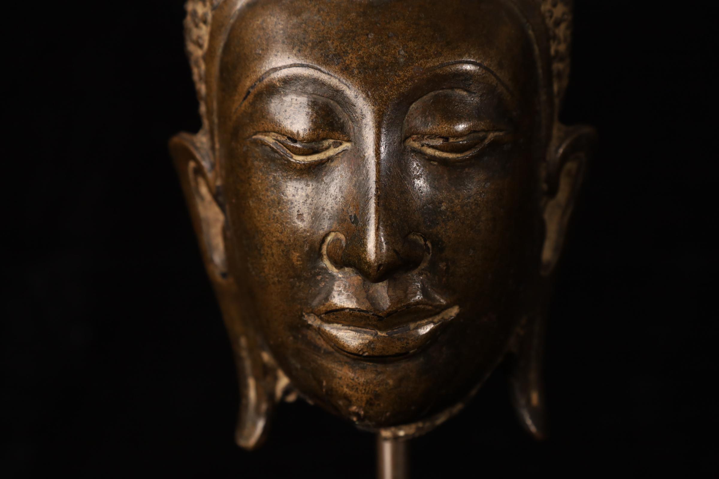 Cabeza de Buda de bronce finamente fundido del reino Uthong, que data de los siglos XIV-XV. Esta elegante pieza refleja la temprana transición estilística hacia la estética de Ayutthaya, caracterizada por una expresión facial serena, cejas