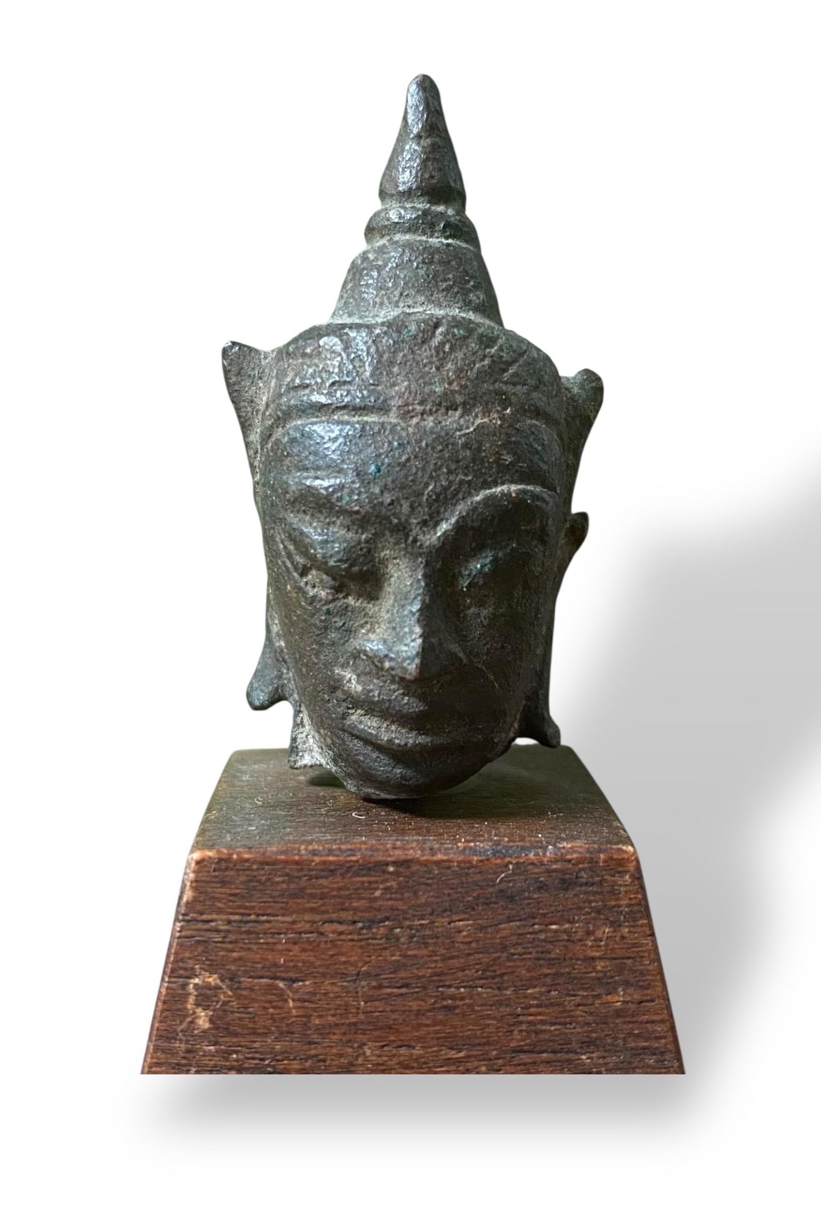 A lovely little bronze Buddha head resting on a wooden base. The brownish-green patina testifies to its age and gives the work an authentic and refined character.

Crafted in Thailand, in the Ayutthaya Kingdom, in the 17th century, this sculpture
