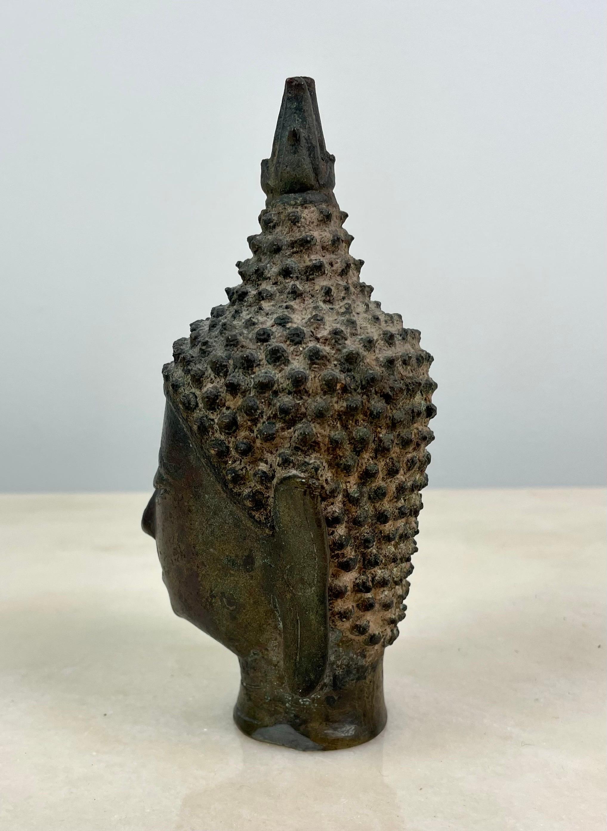 Testa di Buddha, Thailandia, bronzo fuso, fine XIX - inizio XX secolo (periodo Rattanakosin), stile Sukhothai/Ayutthaya. Elegante testa votiva con volto sereno, occhi socchiusi sotto un arco continuo e bocca finemente orlata. I capelli sono resi in