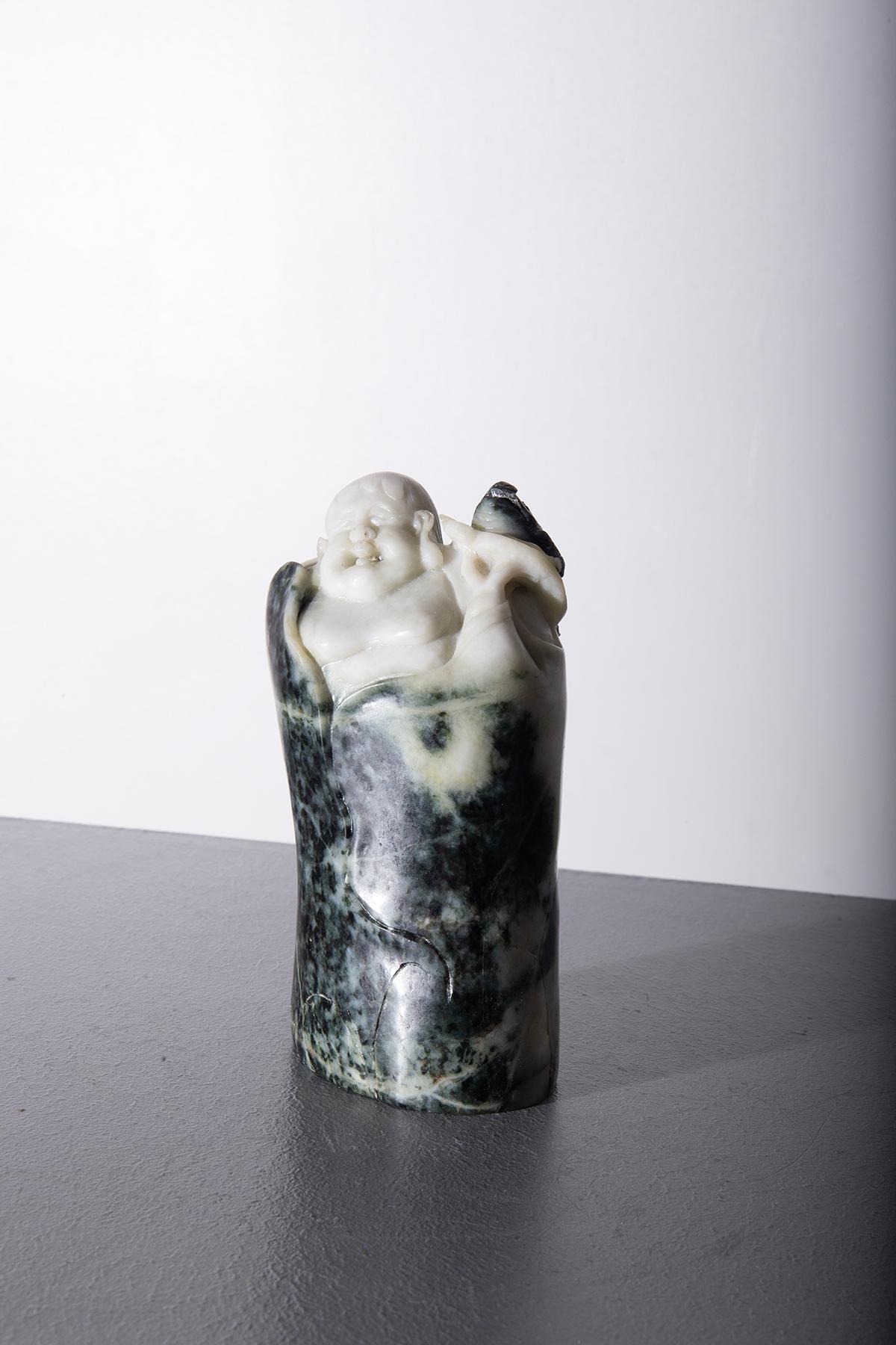 Cette sculpture captivante représente un Bouddha avec une grenouille reposant sur son épaule. Elle est réalisée à partir de racines de jade. Le Bouddha, avec son sourire serein et sa posture détendue, dégage un sentiment de paix et de tranquillité,