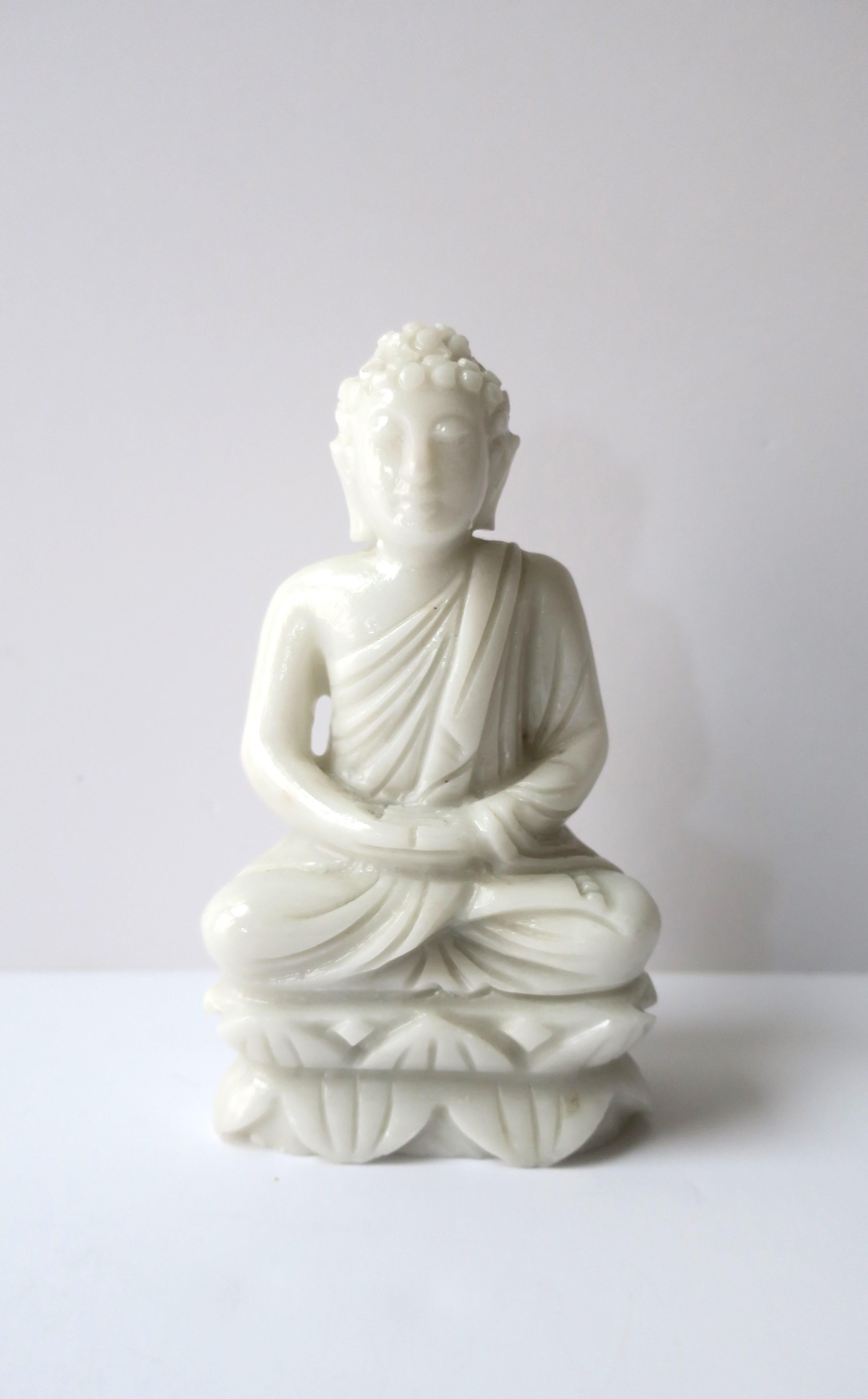 A milk glass Buddha statue sitting in meditating position with lotus leaves surrounding base, circa mid-20th century. There are several special characteristics of a Buddha; specific to this Buddha they include long earlobes. Buddha is adorned with a