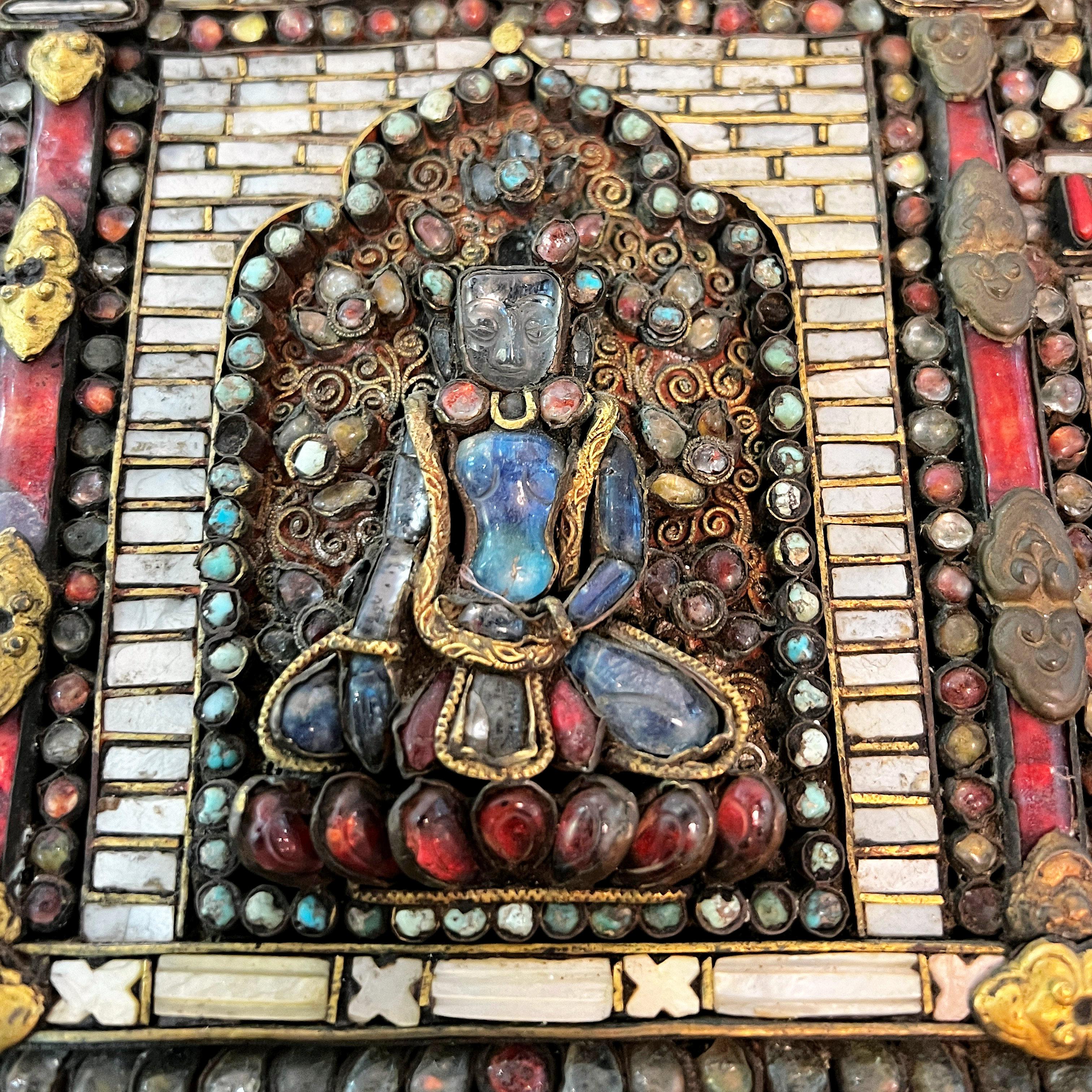 Our exceptional Buddhist votive plaque from Nepal (or possibly Tibet) features the seated figure of Buddha within an intricate mesh of gilt wire inlaid with acquamarine, other semi-precious stones and coral.  Plaques such as this were used at a