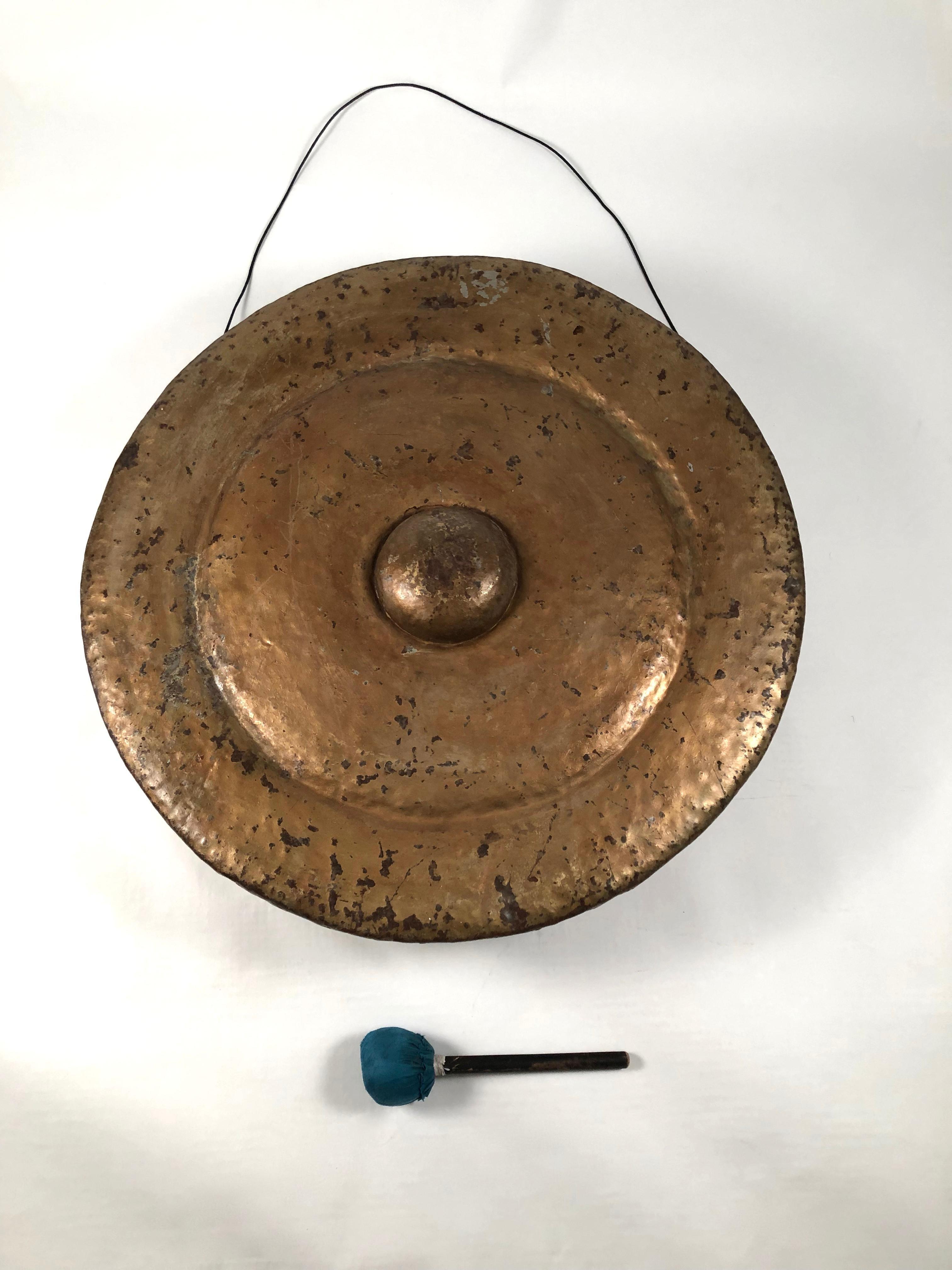 An antique Southeast Asian Buddhist temple gong, likely Thai or Burmese, circa 1890-1910, in gold and black painted riveted metal, of circular form with a projecting circle in the middle, which is the striking point, together with fabric and wood