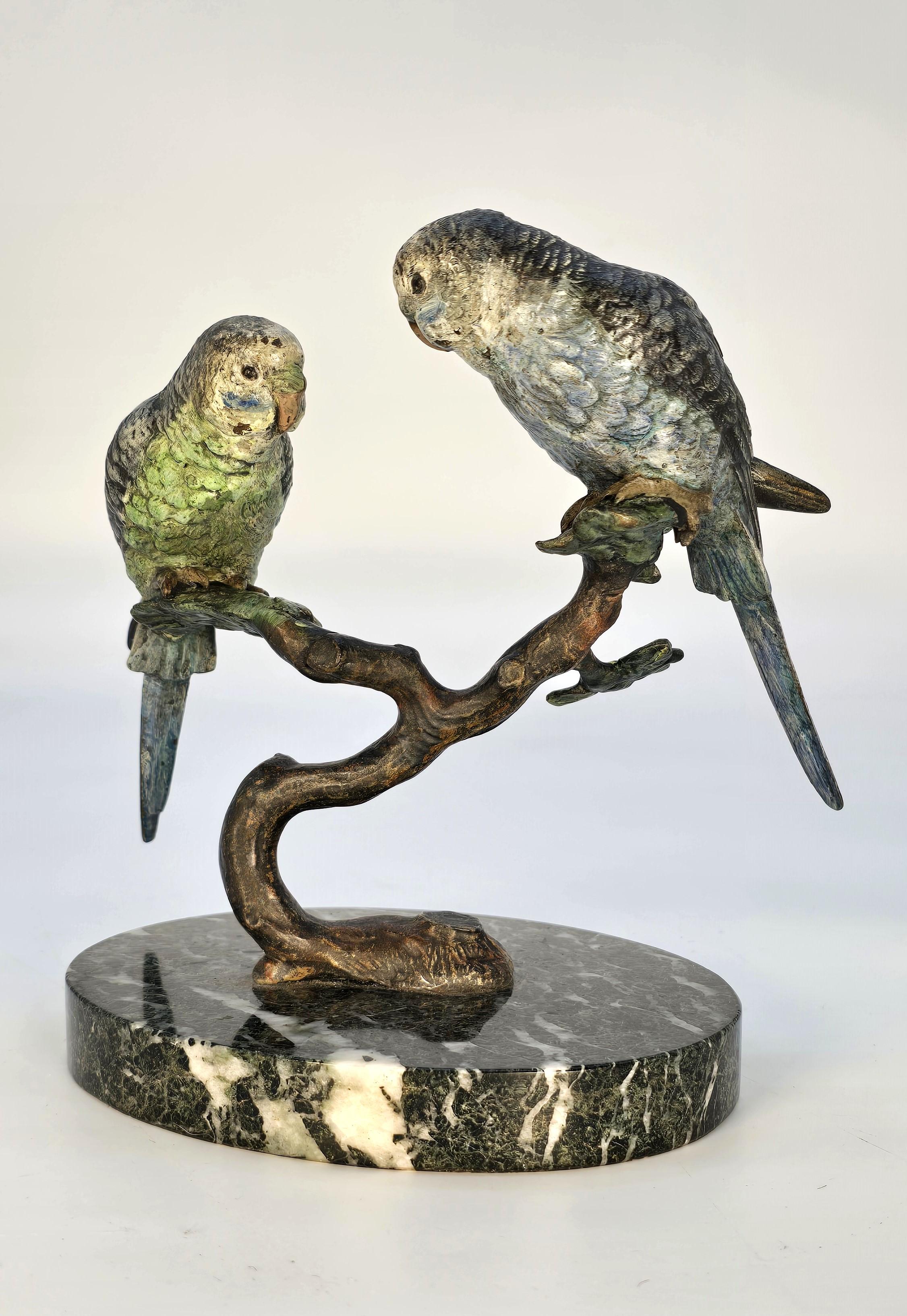 Una superba coppia di pappagallini austriaci in bronzo di grandi dimensioni. Questa impressionante scultura è a grandezza naturale e raffigura due pappagallini, uno verde e l'altro blu, appollaiati su un ramo frondoso. I modelli sono bellissimi, con