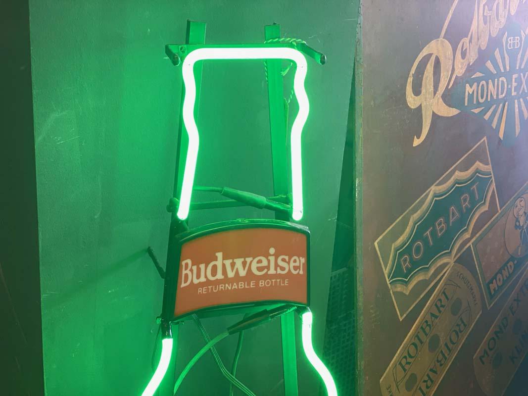 Budweiser Beer neon sign, made in the USA in 1989. The advertising sign consists of bright green and red neon tubes, and two acrylic discs printed with the Budweiser label, which are also backlit. The illuminated object, in the shape of an oversized
