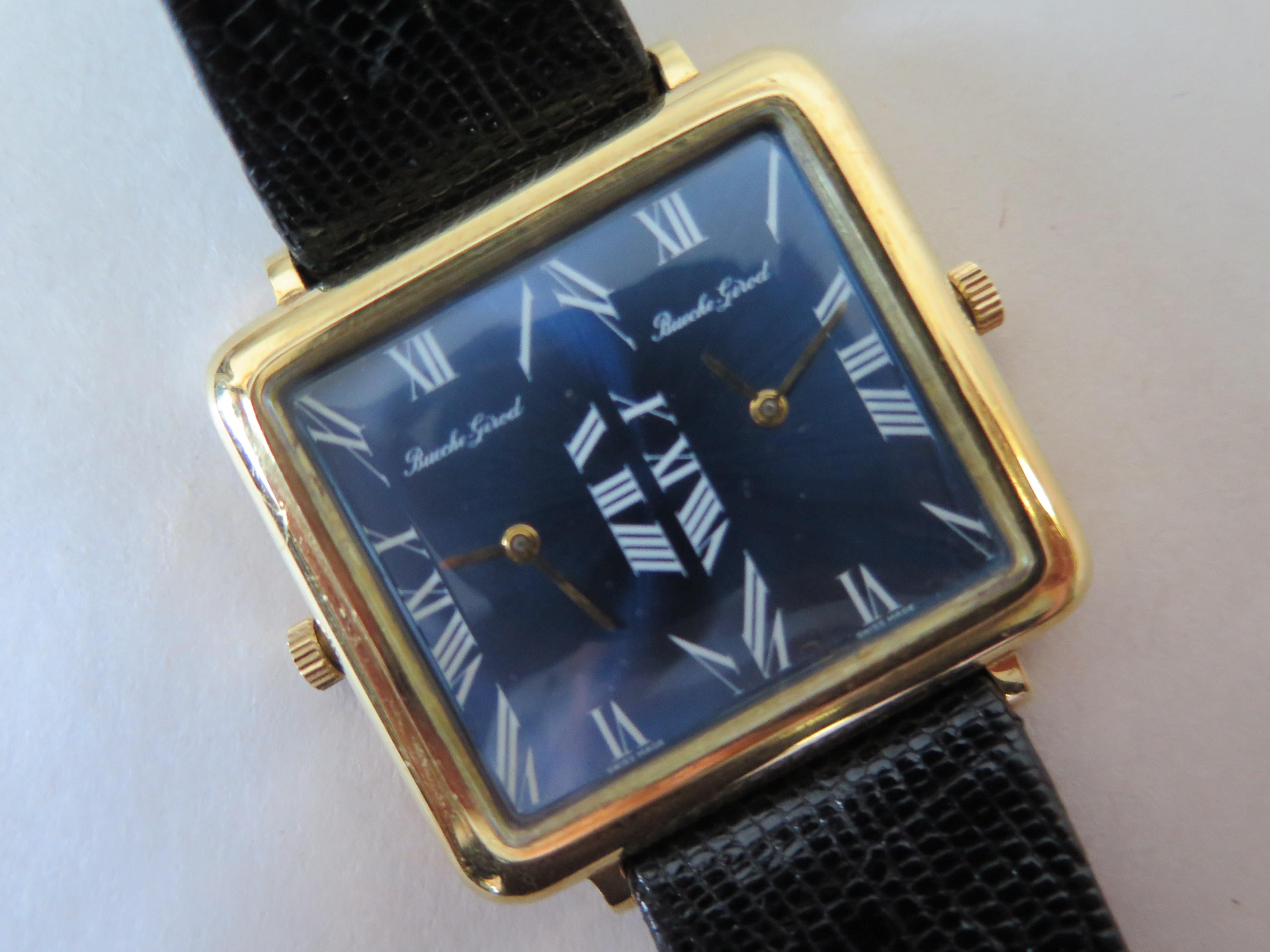 Une montre mécanique à double heure inhabituelle de Bueche Girod en or 18 carats. Le cadran bleu scintille/réfléchit à la lumière vive. La montre a une présence au poignet et un poids substantiels. Elle mesure 32x35 mm, cornes/couronnes non