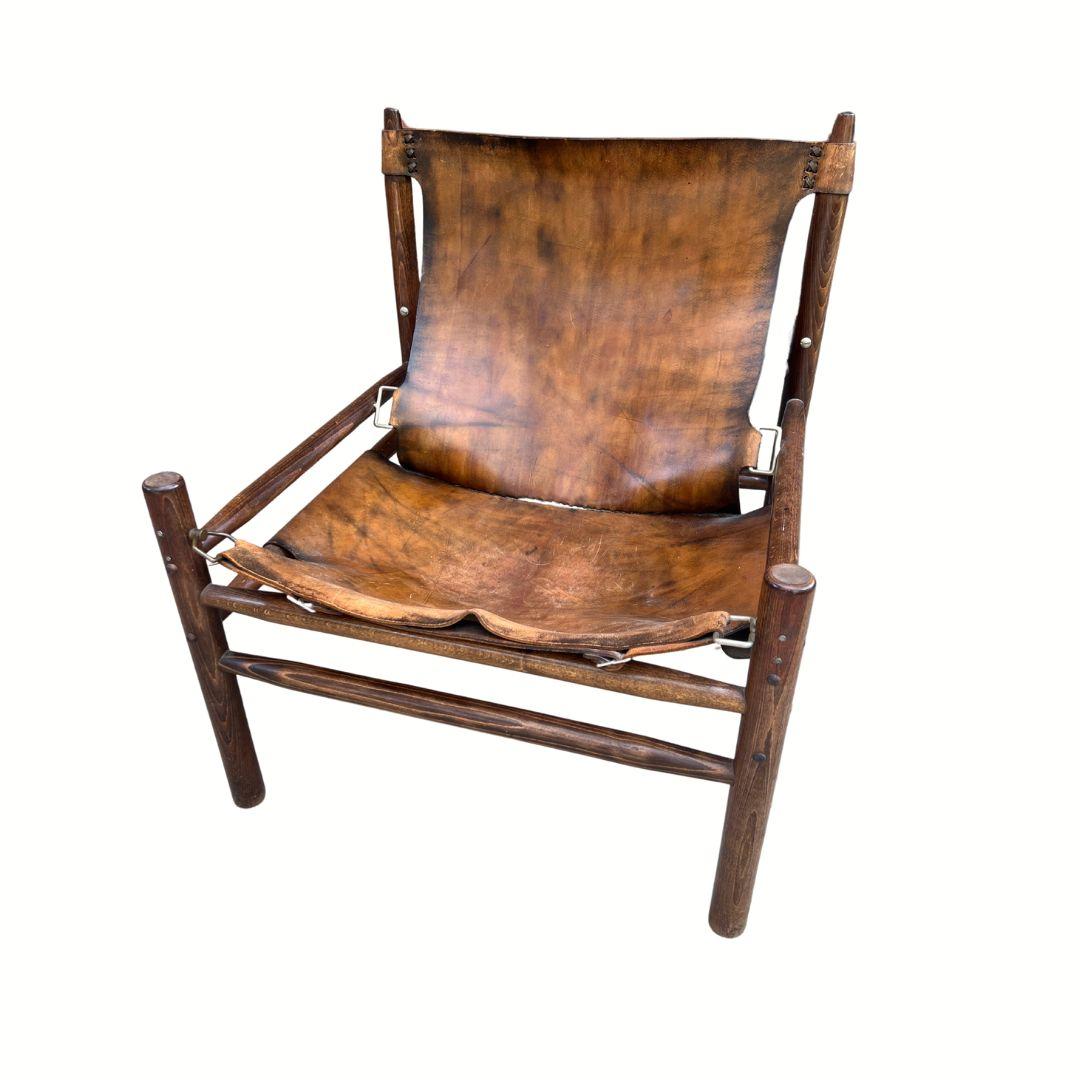 Ce fauteuil de style Safari des années 1970 a une allure classique, avec son riche cuir de buffle et son chêne massif. Le cuir a magnifiquement vieilli et le bois est encore en très bon état.

Son design simple et décontracté s'intègre aussi bien