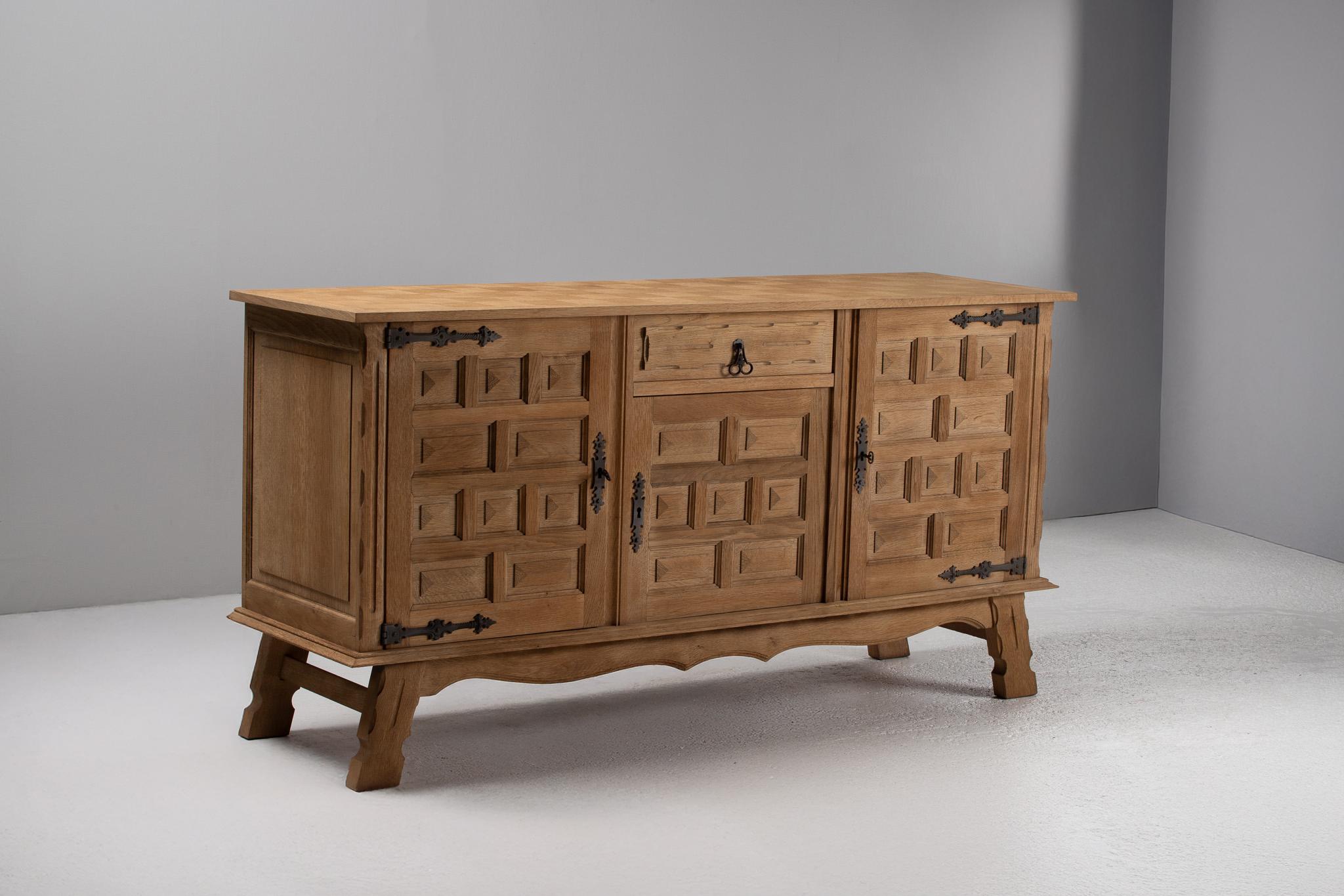 
The silhouette of this sideboard is commanding yet grounded, its architectural rhythm unfolding in quiet repetition across a triptych of doors. Light settles softly across the faceted carvings, catching on each raised panel as though grazing the