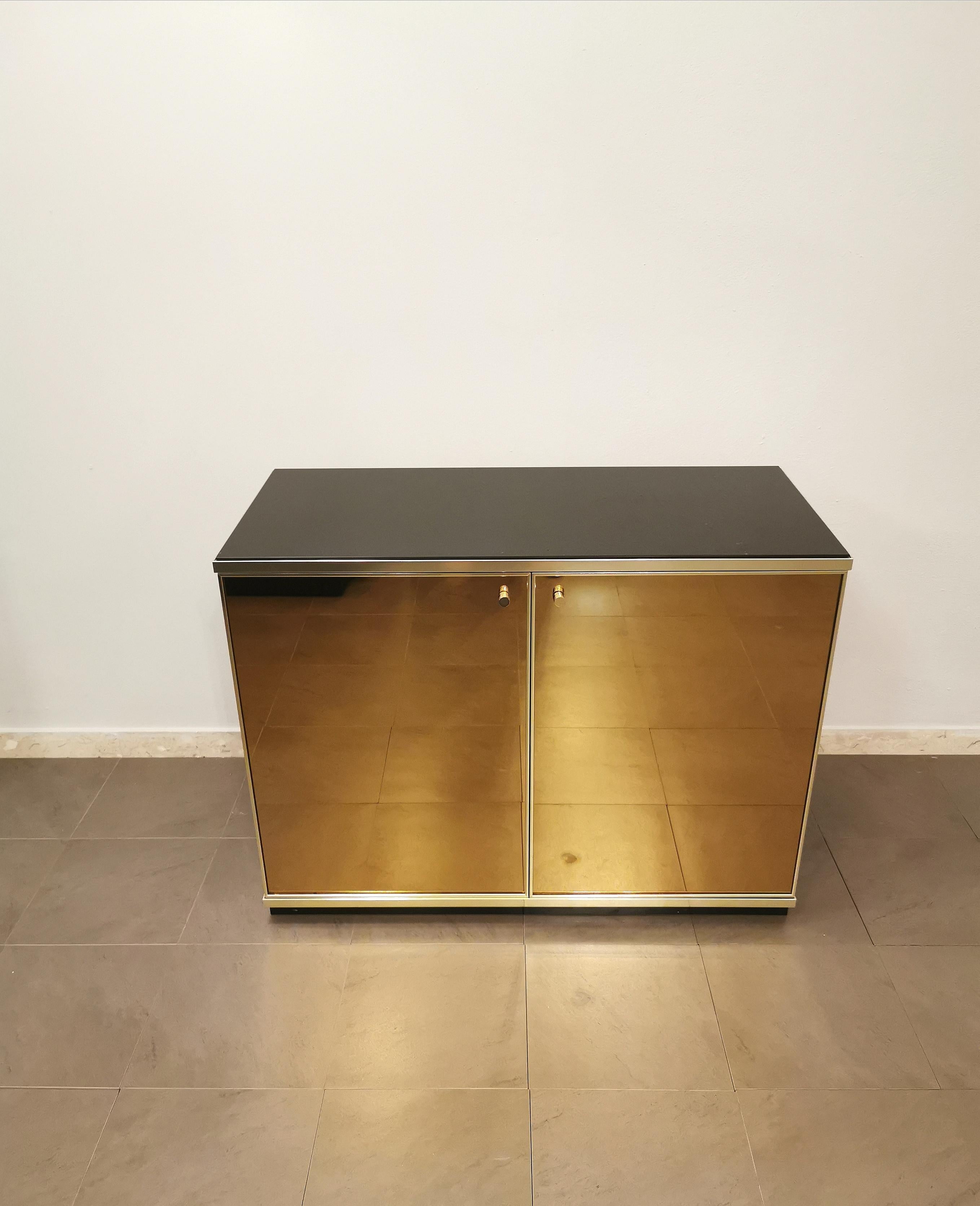 Elegant and rare buffet designed by the Italian designer Renato Zevi in the 70s. The buffet has a black lacquered wooden structure, a dark glass top, 2 bronze mirrored glass doors with sand-colored suede inside and 1 wooden shelf. Finishes in gilded