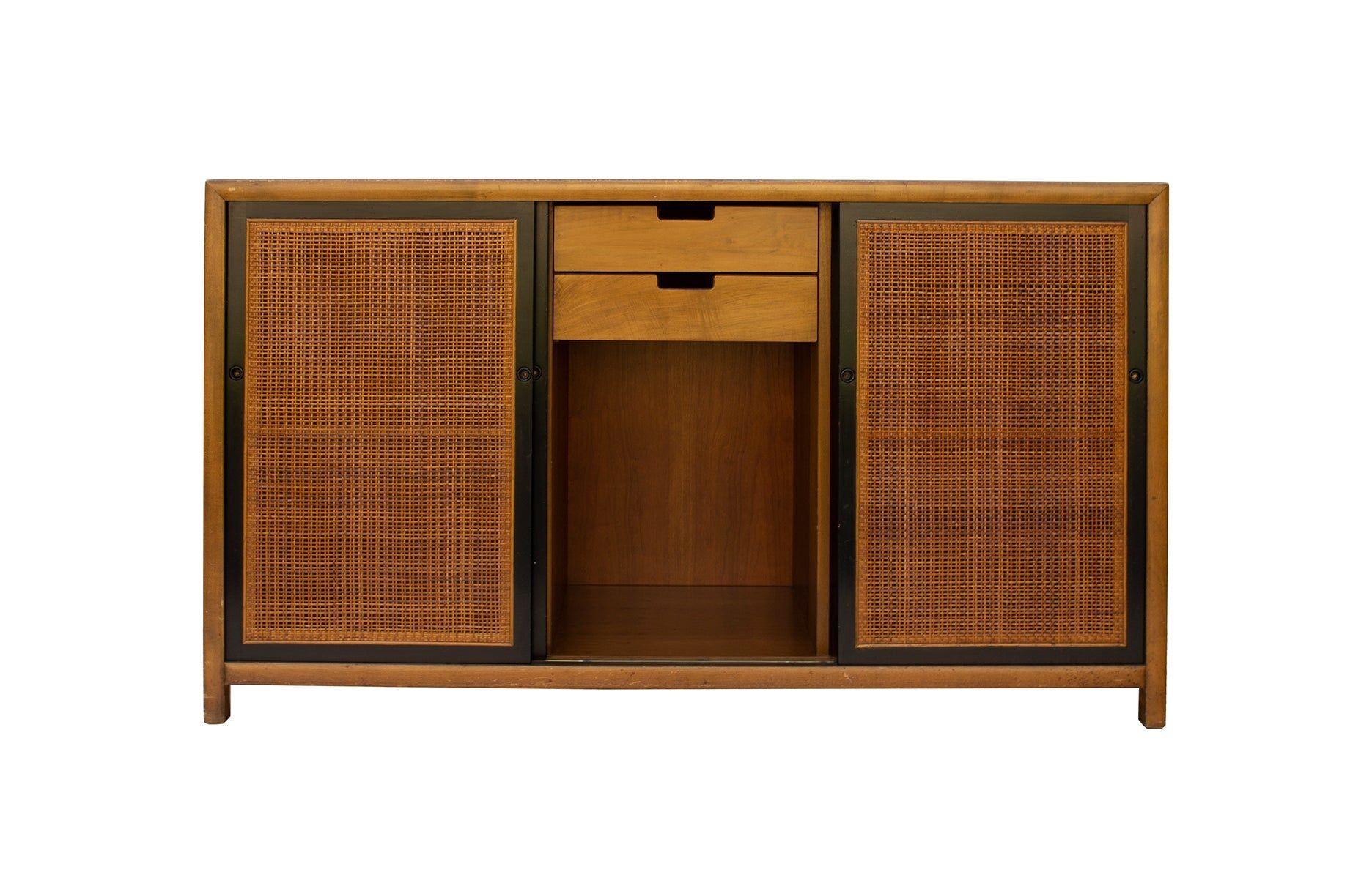 USA, 1960s
Cherry buffet wth ebonized detailing and caned doors designed by Michael Taylor for Baker Furniture. Silver oval tag. A fine amount of storage and texture. Left and right sides of the cabinet each have two fixed position shelves; center