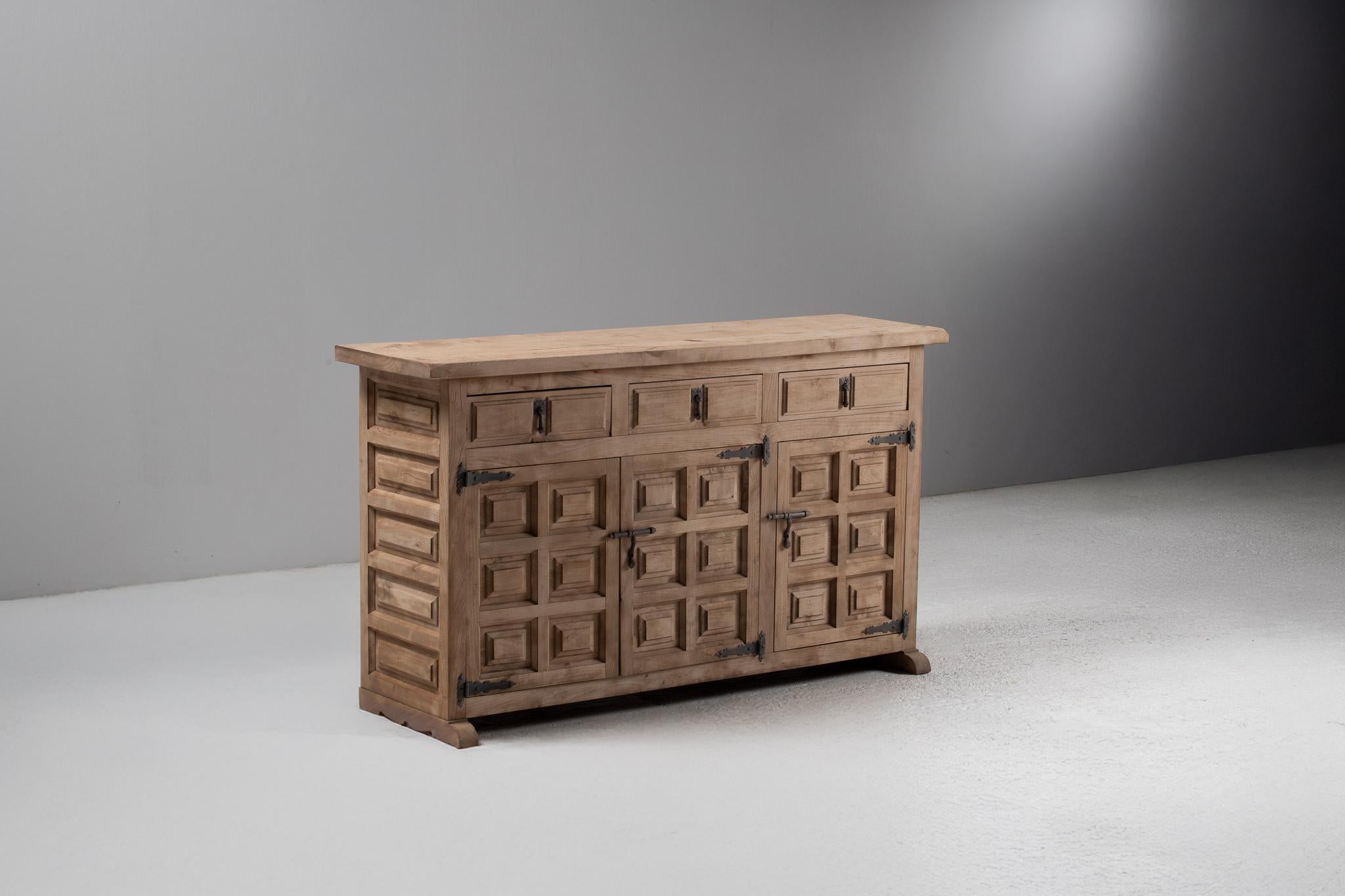 Dieses Buffet aus spanischer Ulme bietet mit seiner beeindruckenden Geometrie und seiner ungeschminkten Ernsthaftigkeit eine skulpturale, in der Tradition verankerte Präsenz. Jede Fassade - bestehend aus erhabenen quadratischen Paneelen - liest sich