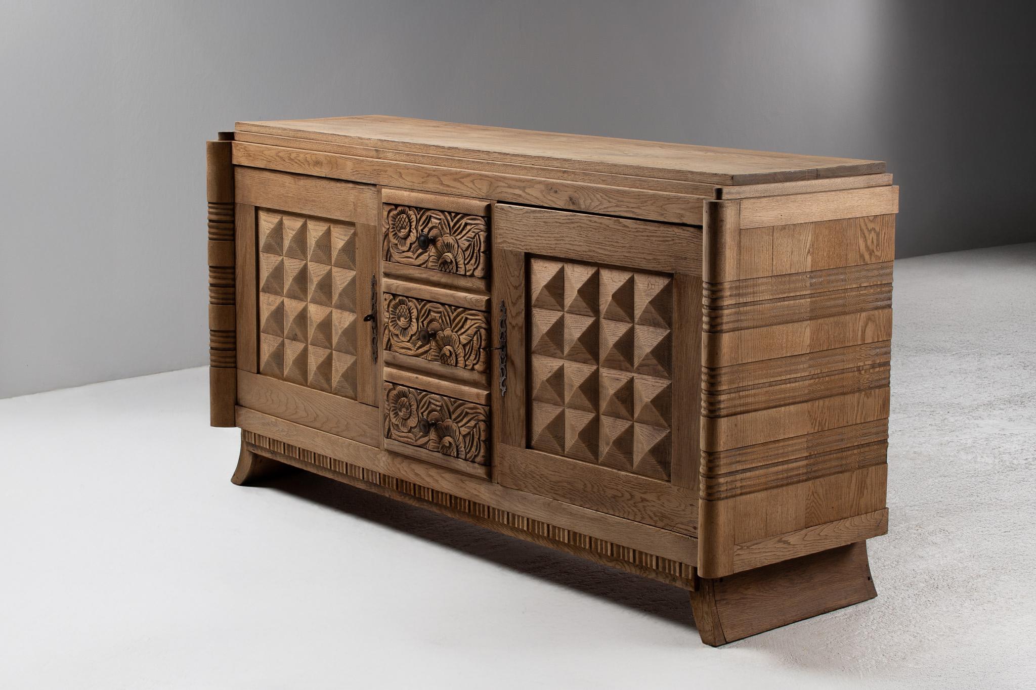 A harmony of ornament and volume, this oak buffet unfolds like a sculptural frieze—each surface a study in geometric tension and botanical exuberance. Flanking doors are crisply faceted with pyramidal reliefs, their rhythm precise and architectural.