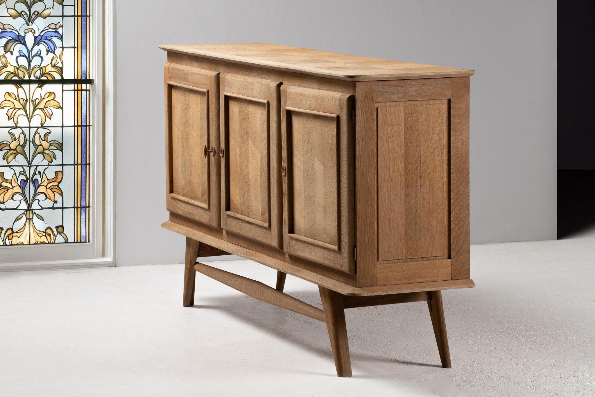 Elevated on tapered legs with the quiet poise of modernist intention, this buffet possesses a restrained elegance—its form at once aerated and architectural. The three-panel façade is distinguished by a rhythmic chevron parquetry, framed within