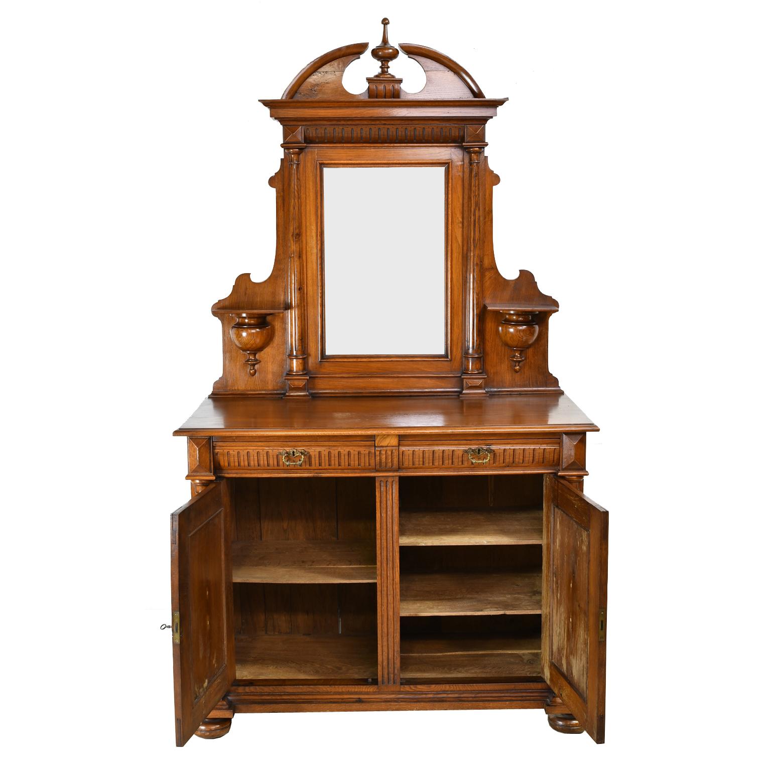 A lovely buffet in oak with a mirrored top over a cabinet with two drawers and two doors. Mirror frame has a split-pediment top with turned center finial and is flanked by fluted columns, with sconces for candles. The cabinet has convex fluted