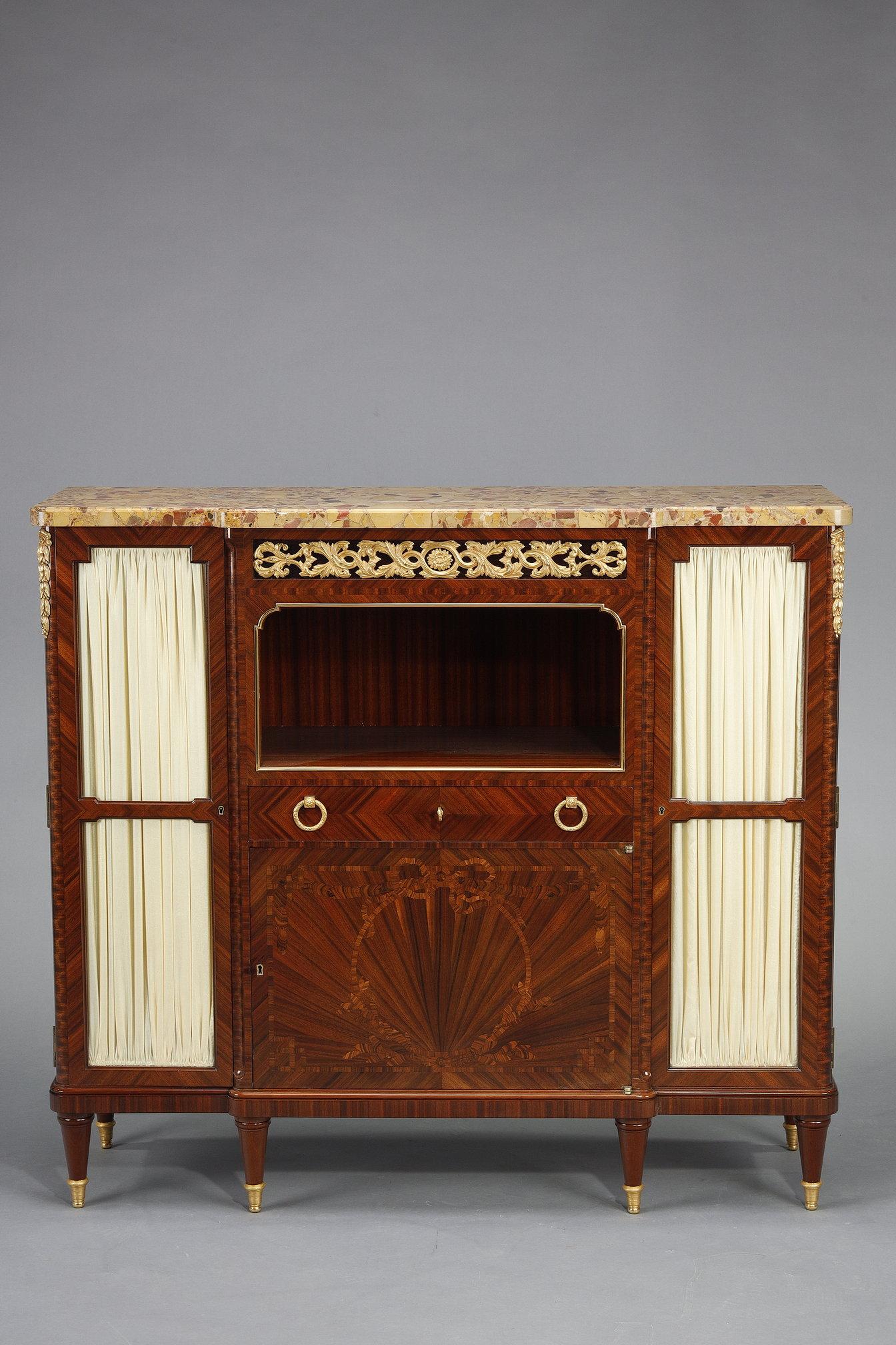 A buffet or low bookcase in veneered wood, opening through a central door with inlaid frieze decoration, topped by a drawer and a niche, and on the sides, through two glazed side doors clad in cream veiling to conceal the contents. The cabinet is