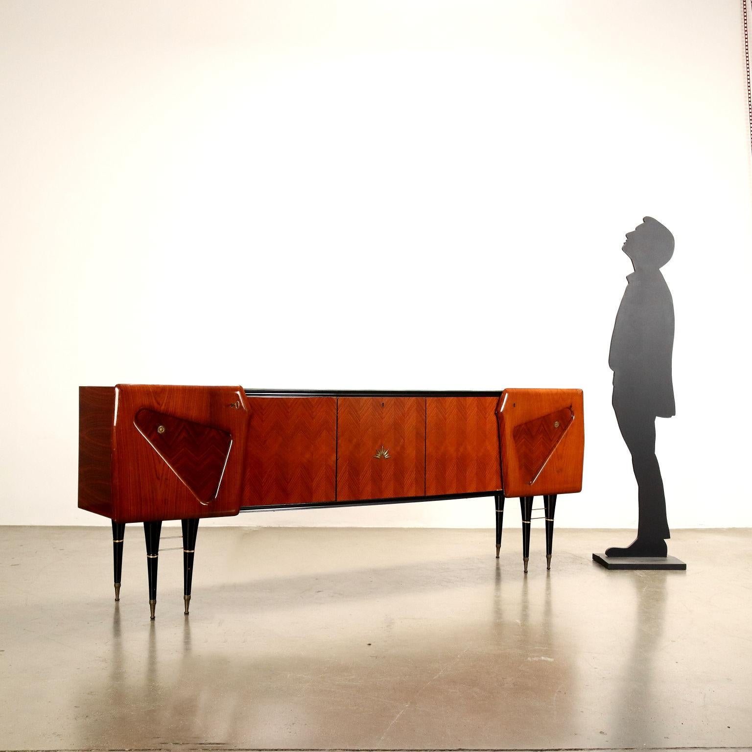 Buffet con aperture a battenti. Legno impiallacciato legno esotico con finitura al poliestere, piano in vetro retro trattato effetto marmo, puntali delle gambe e particolari in ottone. 