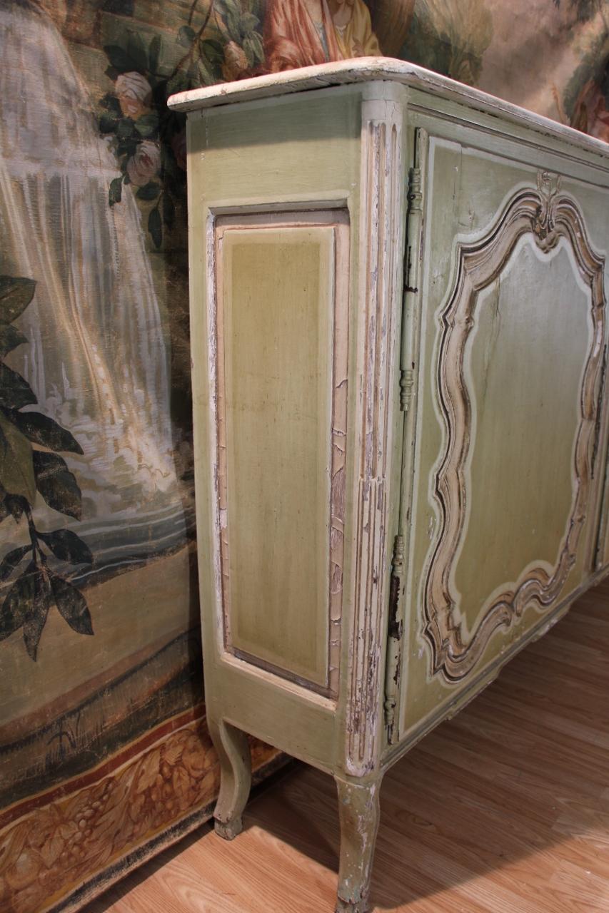 furniture at support height in carved wood re-lacquered green, opening with two leaves carved with scalloped reserves, fluted uprights, curved crowbars, wear and damage to the paintwork, lock not original
