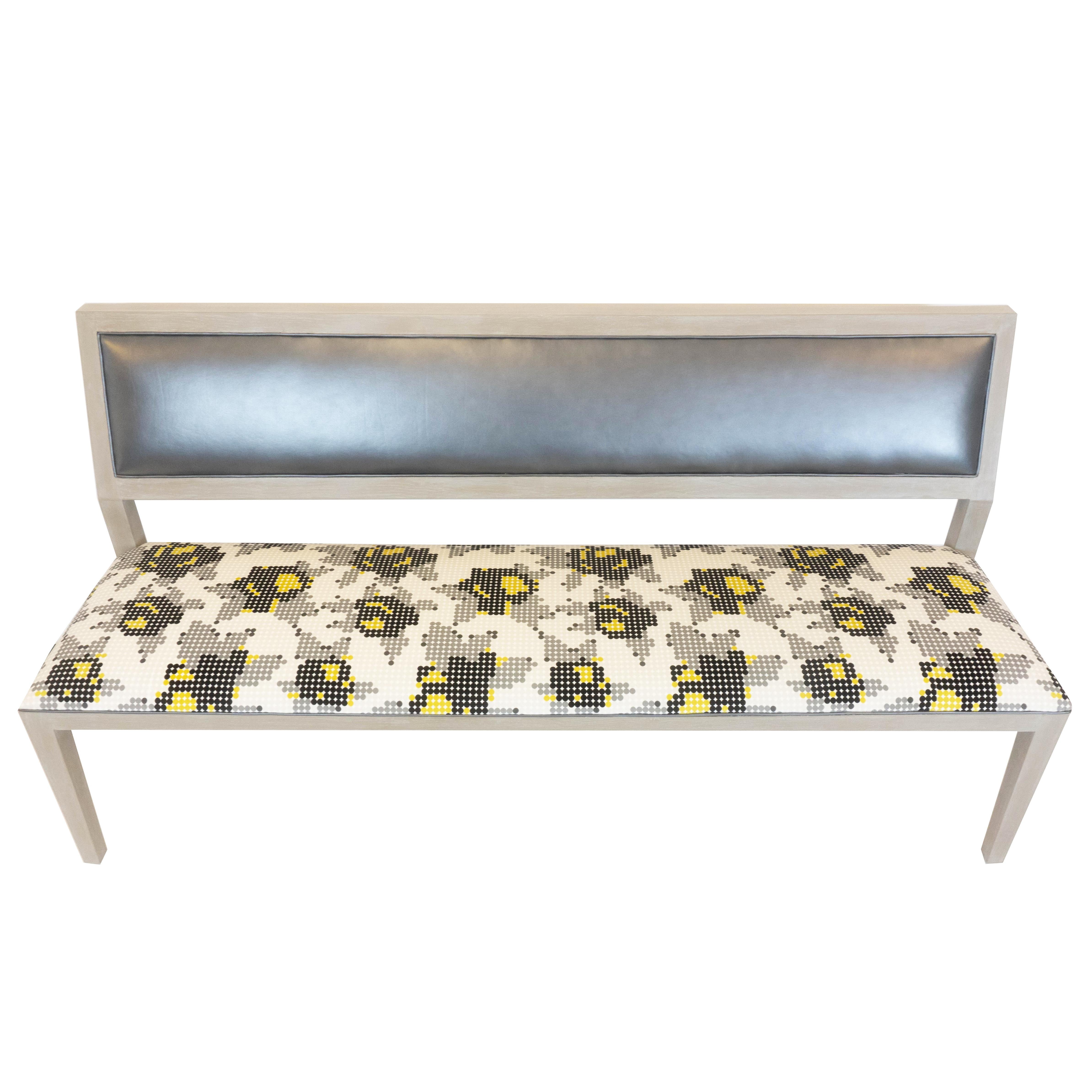 Our built to order bench is completely customizable. The bench shown has a cushioned back that is upholstered and welted with a grey vinyl material, the padded seat is upholstered in a pixel-like floral print, and the exposed wood is done in a
