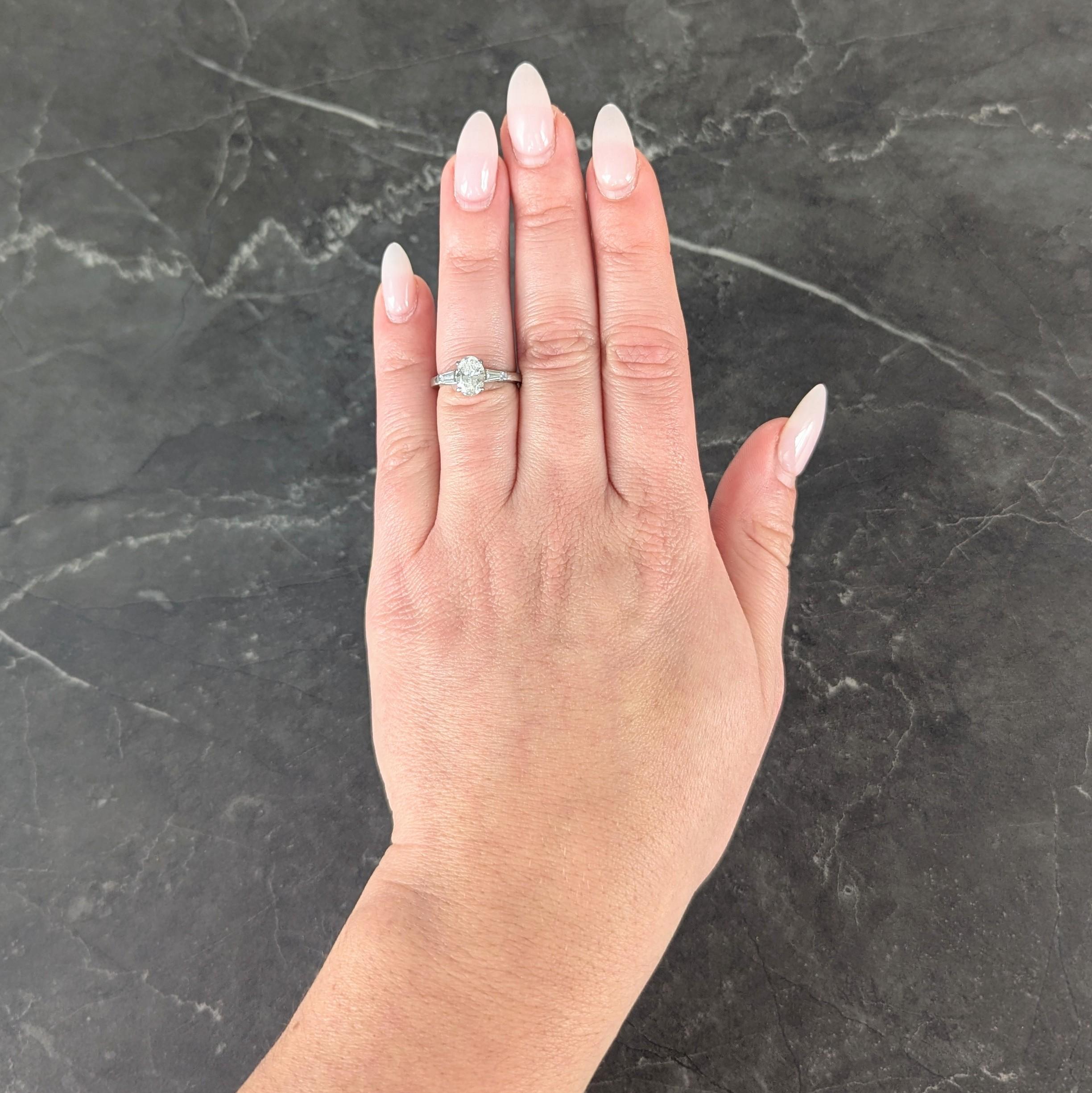 Centering an oval cut diamond weighing 1.10 carats - F color with VVS2 clarity
Prong set in basket and flanked by cathedral style shoulders
Bare set with tapered baguette cut diamonds
Weighing approximately 0.26 carat total
Well matched to