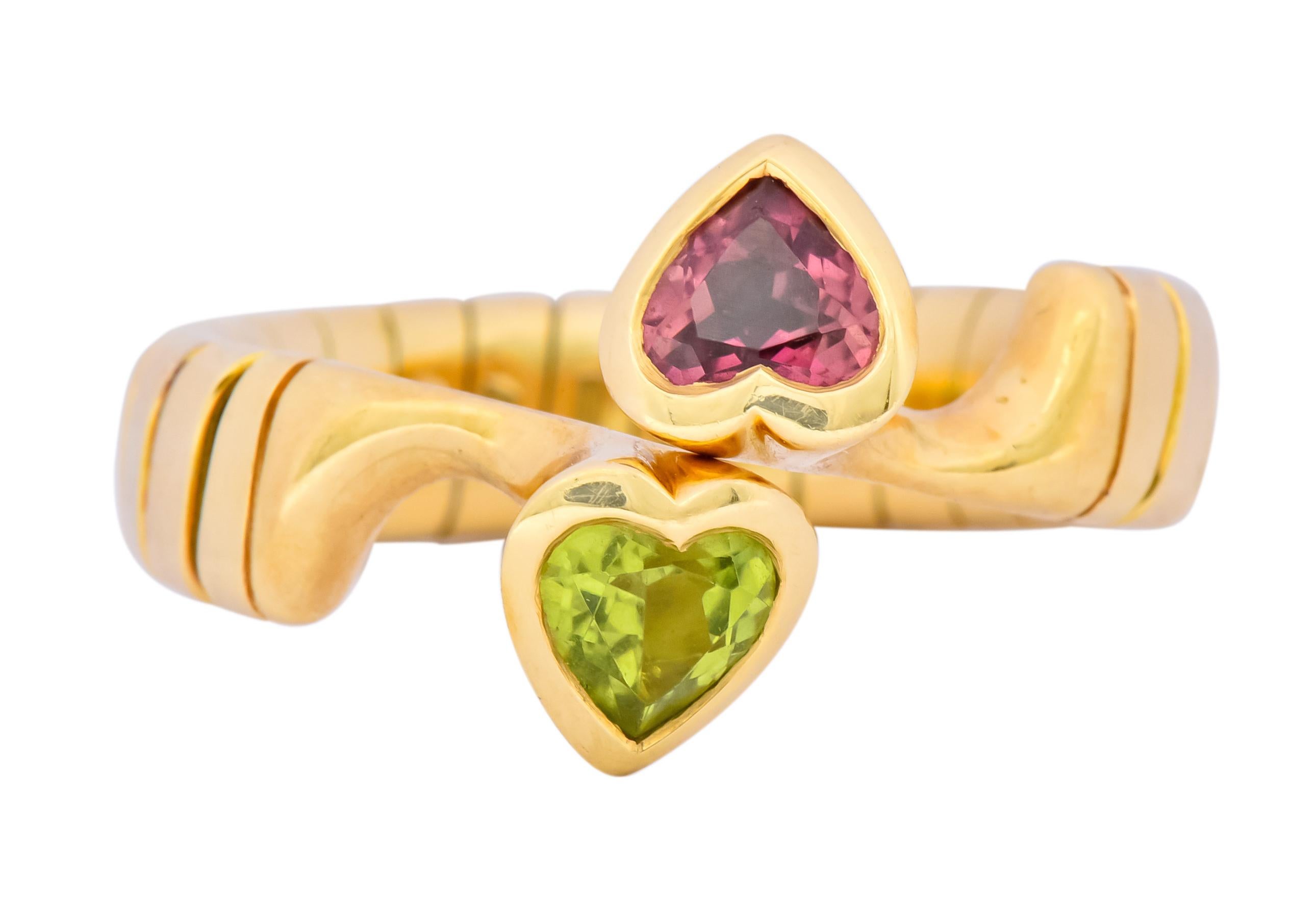 Centering heart cut pink tourmaline and peridot, weighing approximately 1.50 carats total and very saturated color

Each bezel set in a polished gold surround in a bypass style ring

Completed by tubogas shank

Fully signed Bvlgari with Italian