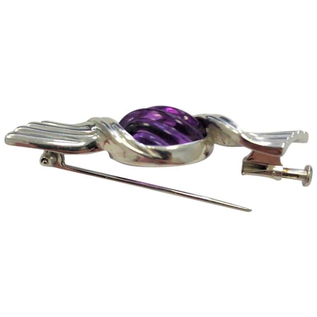Bulgari 18 Carat White Gold And Amethyst Sweet Wrapper Brooch. Designed as a sweet wrapper with the carved cabochon amethyst between white gold wrapper. Signed 'Bulgari' and '750'. Weighing 10.4 grams and approximately 4.9 centimetres in length.