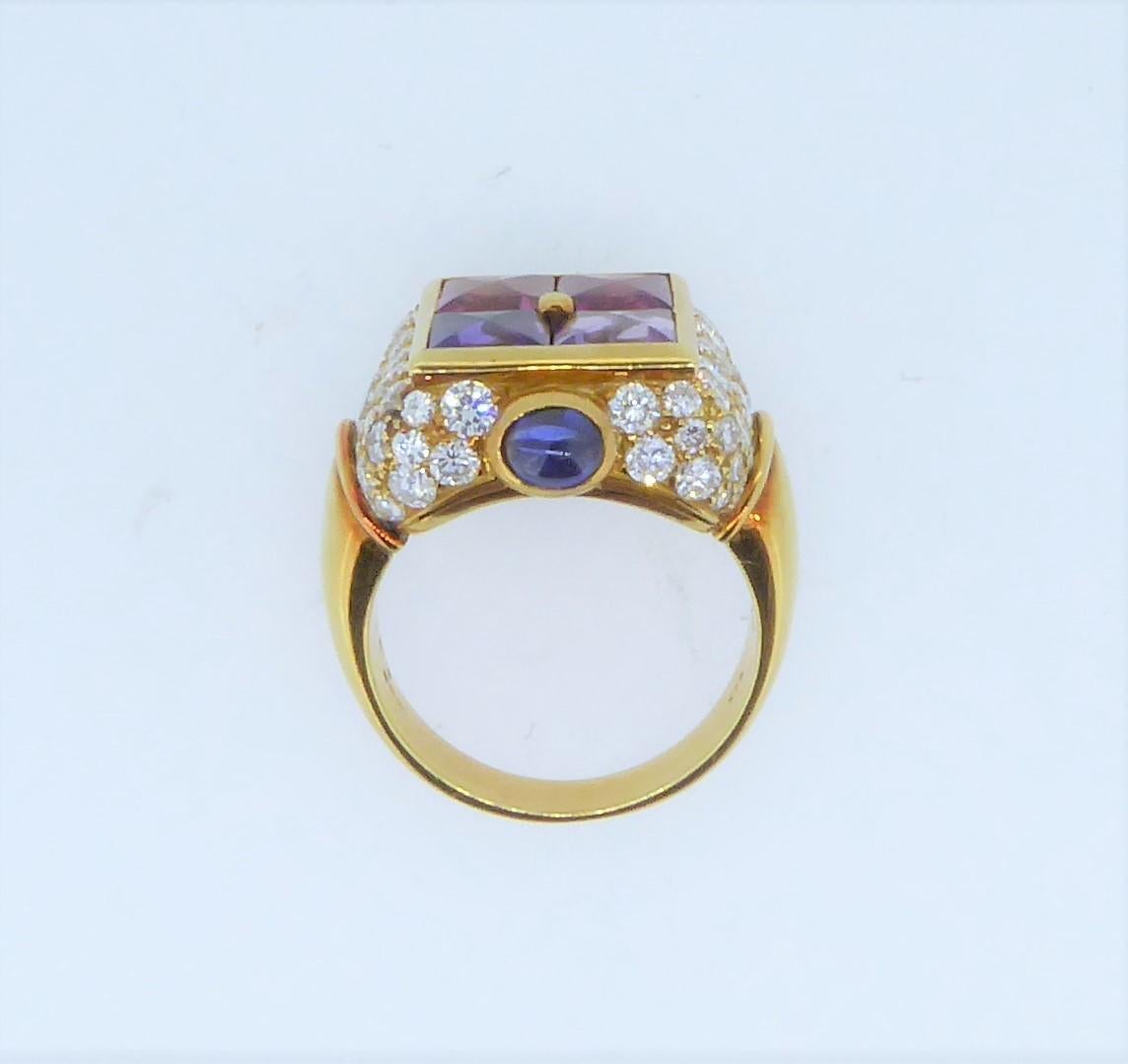 A Bulgari 18 Carat Yellow Gold Multi-Gem And Diamond Carré Ring. 
The ring adorned with amethyst, topaz, tourmaline and cabochon sapphires within a pavé-set diamond border. Signed 'Bulgari' '750' and numbered. Weighs approximately 12.2 grams. Finger