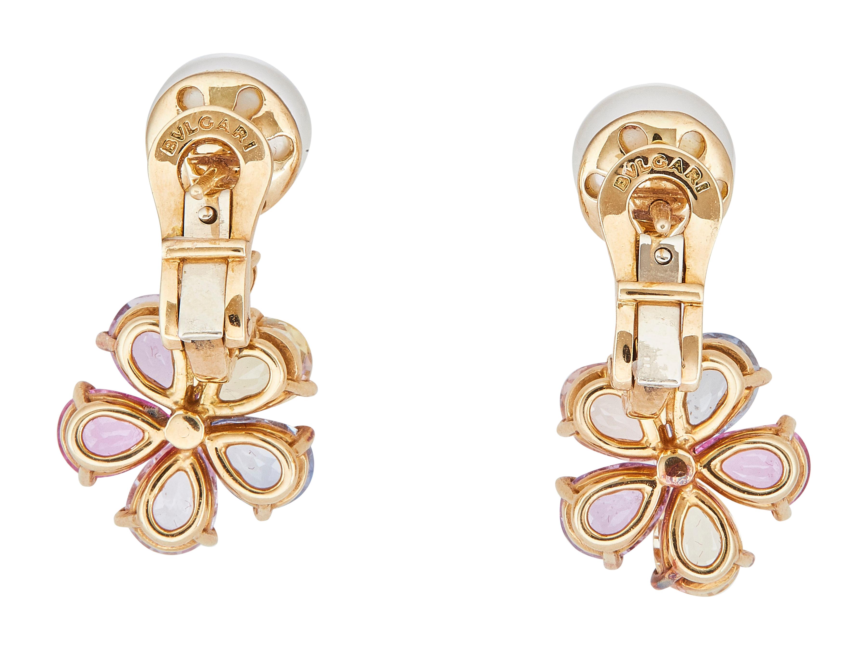 The earrings: A pair of Bulgari eighteen karat yellow gold, multi-hue sapphire, pearl and diamond earrings. Each designed as a sapphire flower head, centered by a diamond and surmounted by a pearl.

The earrings are in excellent condition, with only
