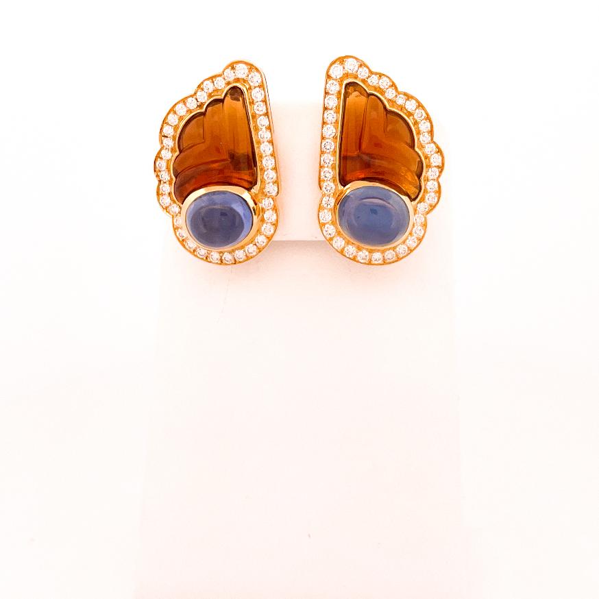From the designer Bulgari, these 18 karat yellow and white gold citrine and blue sapphire wing earrings. This design was crafted with 2 bezel set oval cabochon cut blue sapphires with an approximate combined weight of 13.74 carats. There are 2