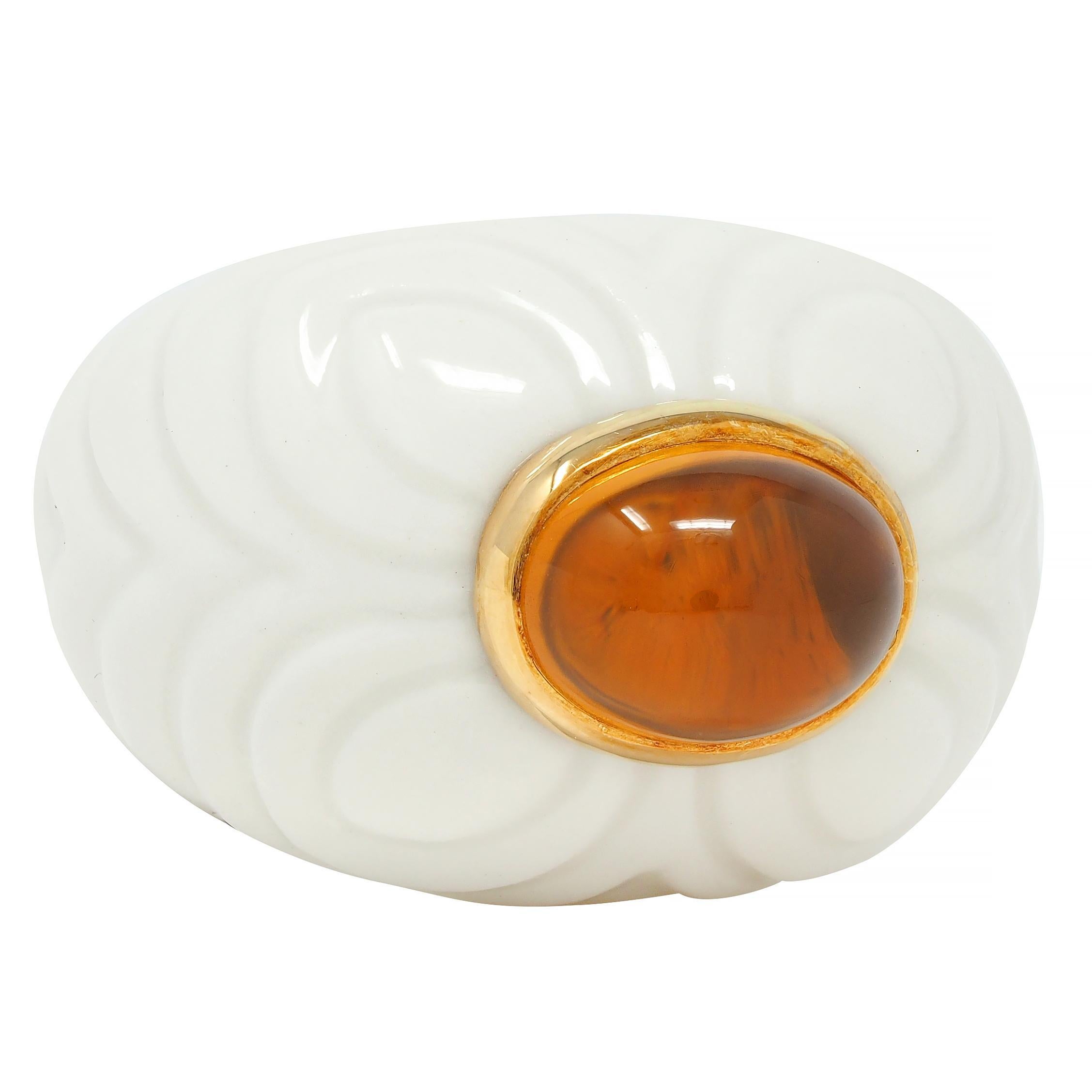 Centering an oval-shaped citrine cabochon measuring 7.5 x 10.5 mm
Transparent medium brownish orange - set east to west in gold bezel
Set atop a domed bombé shaped porcelain ceramic form 
Grooved with a tiered quatrefoil petal motif
Opaque glossy