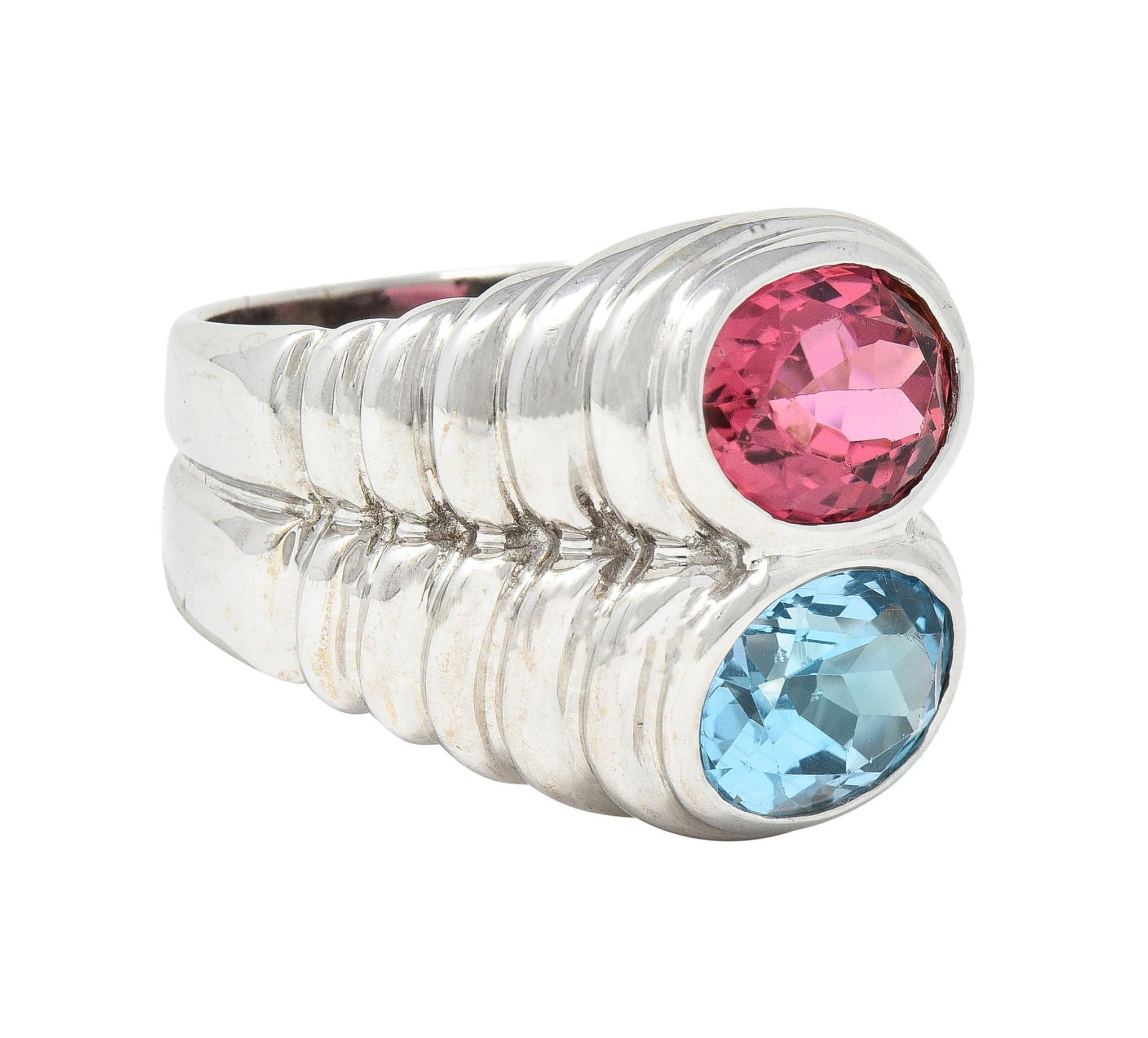 Featuring an oval cut topaz and tourmaline bezel set north to south 
Topaz weighs approximately 2.40 carats - transparent light blue
Tourmaline weighs approximately 1.89 carats 
Transparent medium orangey-pink 
With domed fluted gallery 
Stamped for