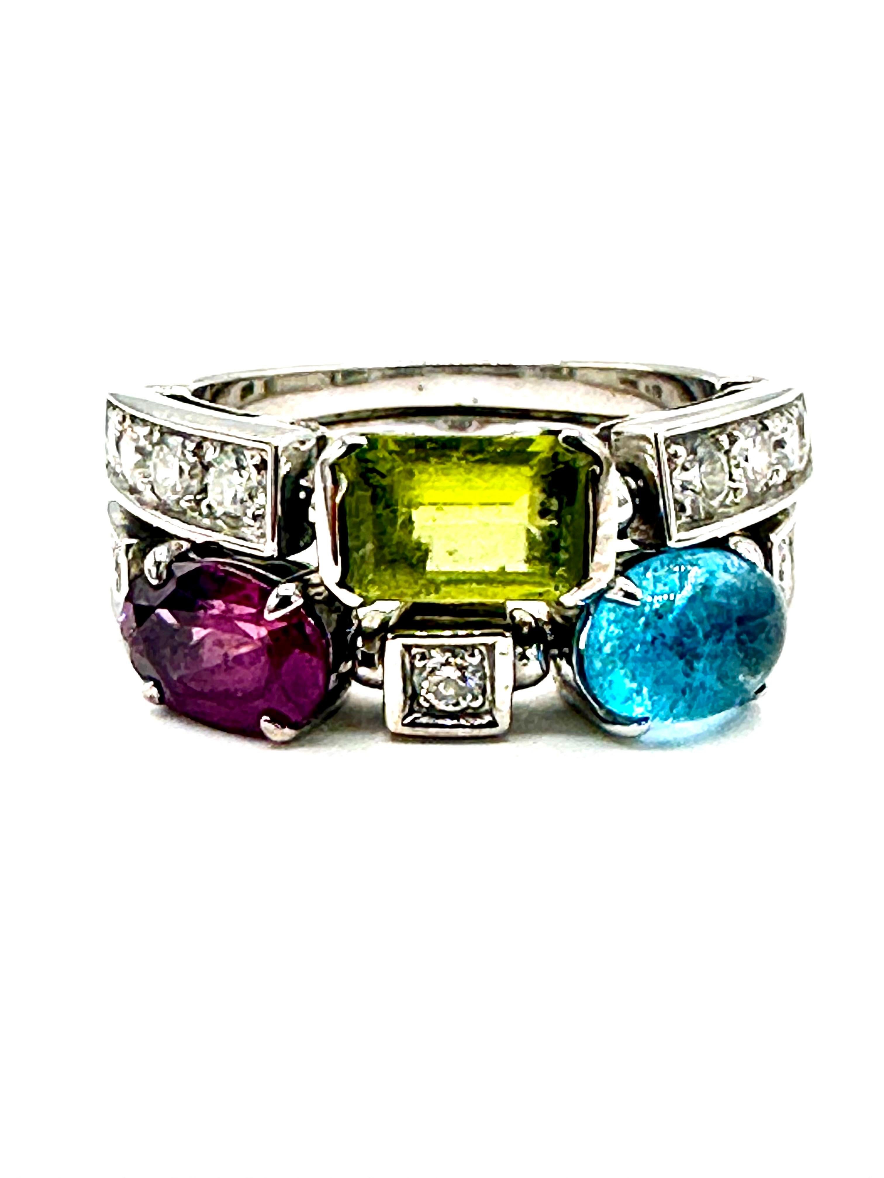 A beautiful 18k white gold multi gem set dress ring from the Bulgari Allegra collection. The ring is of split design, set with a 1.00ct emerald cut peridot, 0.70ct cabochon blue topaz and 0.65ct oval cut pink rhodonite garnet, complemented by pave