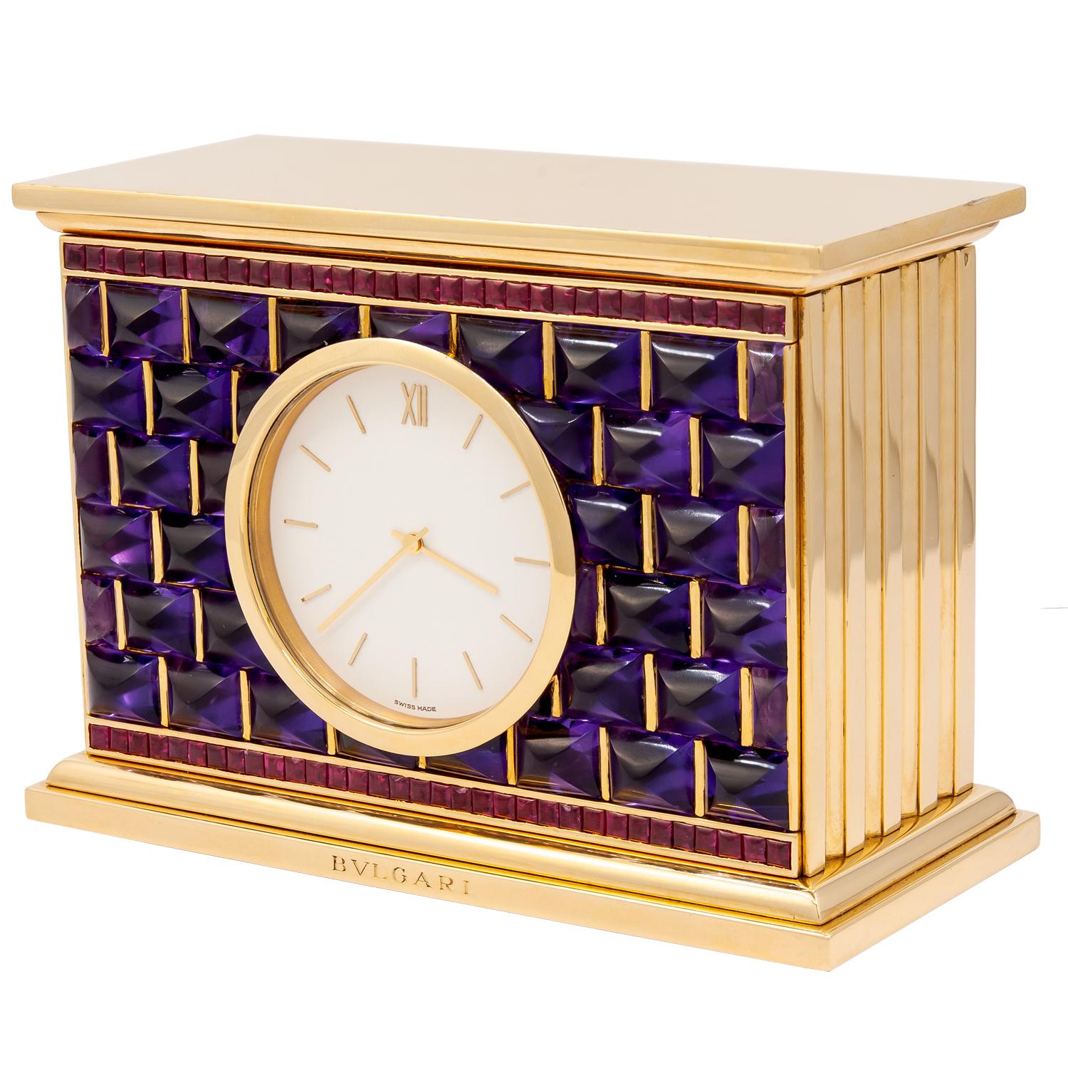 Bulgari Rome 1980s Cabochon Amethyst Ruby 18Carat Gold Iconic Style Desk Clock
An 18k yellow gold quartz desk clock, set with  shaped amethyst bordered by rubies, signed Bvlgari.
measures approx.  3.5″ in length x 1.65″ in width x 2.5″ in