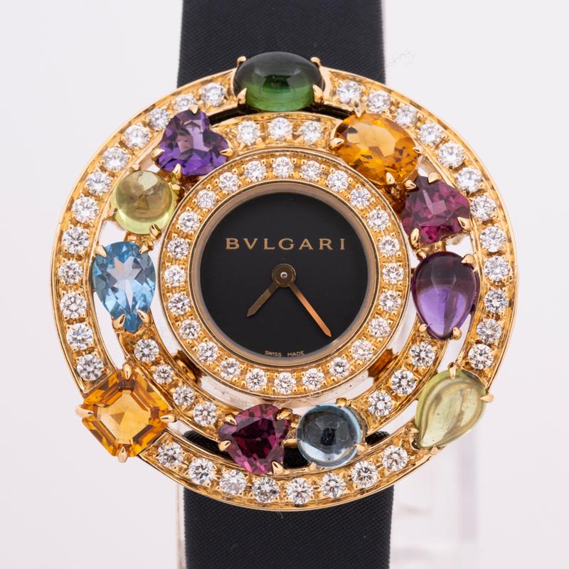 A stunning Astrale Cerchi wristwatch in yellow gold by Bvlgari, featuring a black dial. Complimenting the dial are 66 round brilliant diamonds and several other multi gemstones including a dark green tourmaline, amethyst, blue topaz, pink