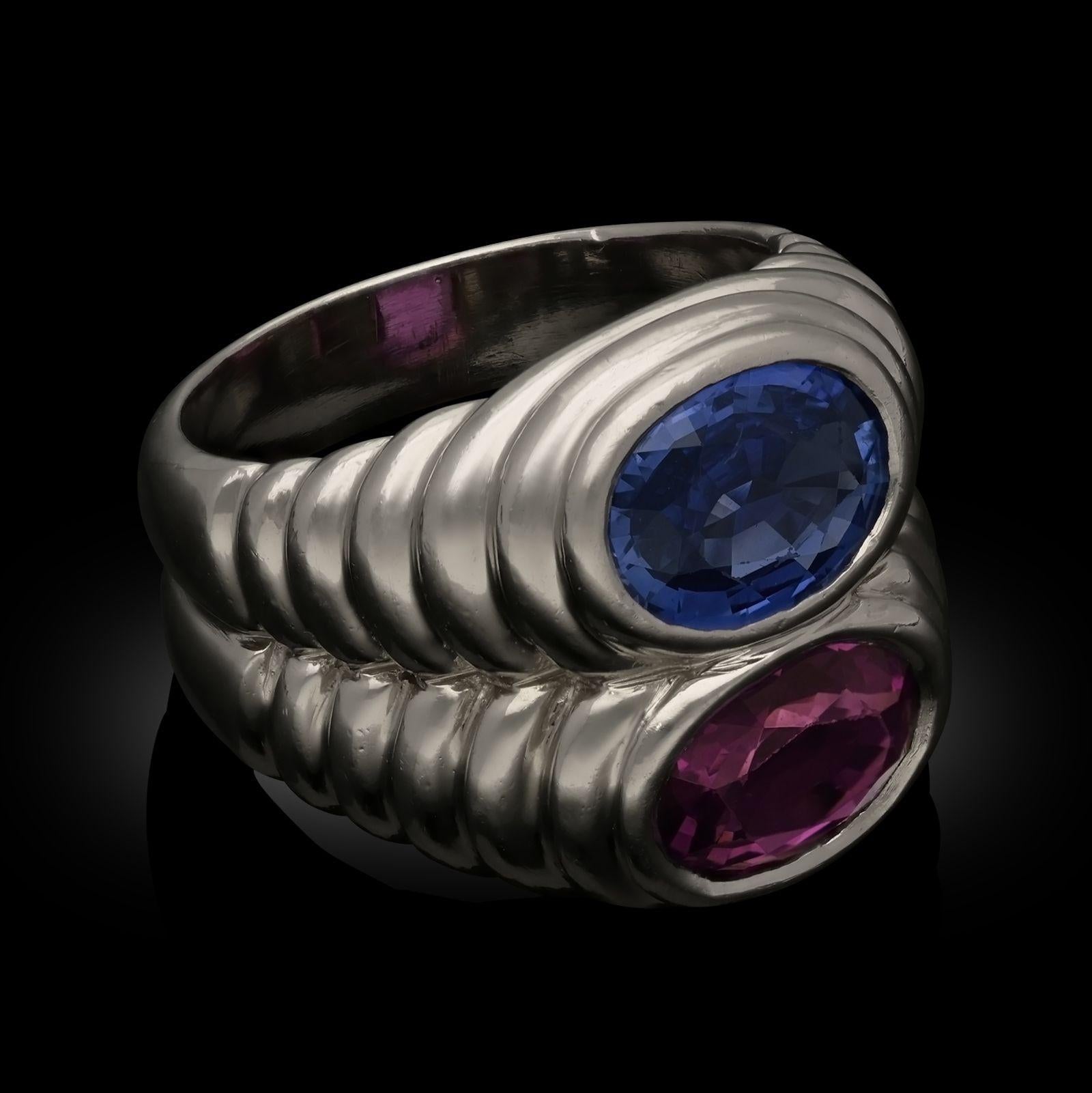 A double sapphire and platinum 'Doppio' ring by Bulgari circa 1980. The natural fancy pink and blue sapphires, both oval cut, estimated at approximately 1.62ct and 1.61ct both unheated, are both set east-west in a platinum ring with fluted